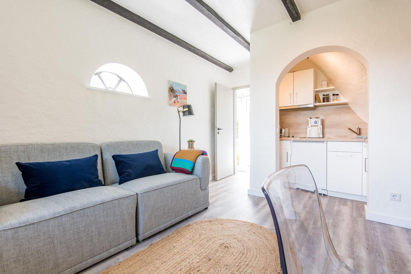Wohnbereich mit Sofa, runder Teppich und Durchgang zur Küche.