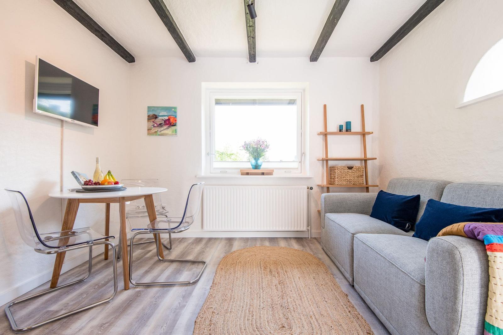 Wohnzimmer mit Sofa, Esstisch und Fenster. Deckenbalken und Holzboden.