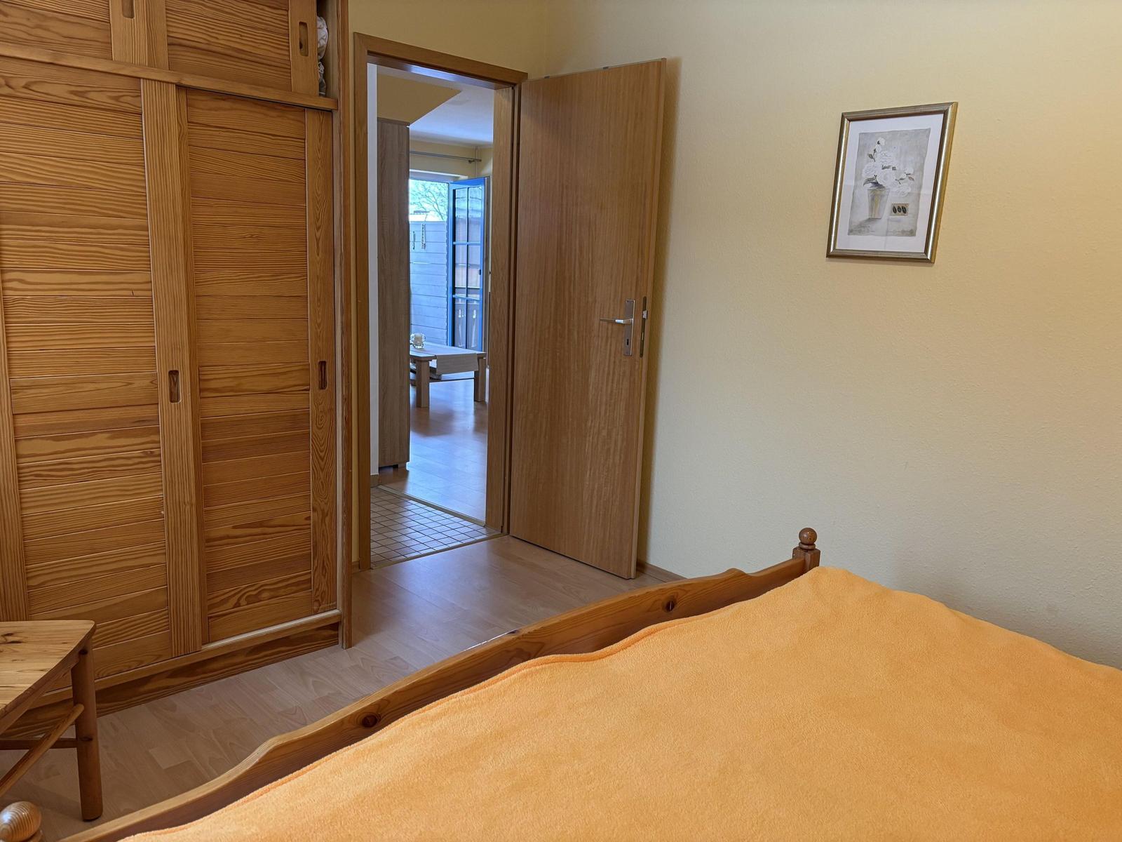 Schlafzimmer mit Holzbett, Schrank und Blick in Wohnbereich.