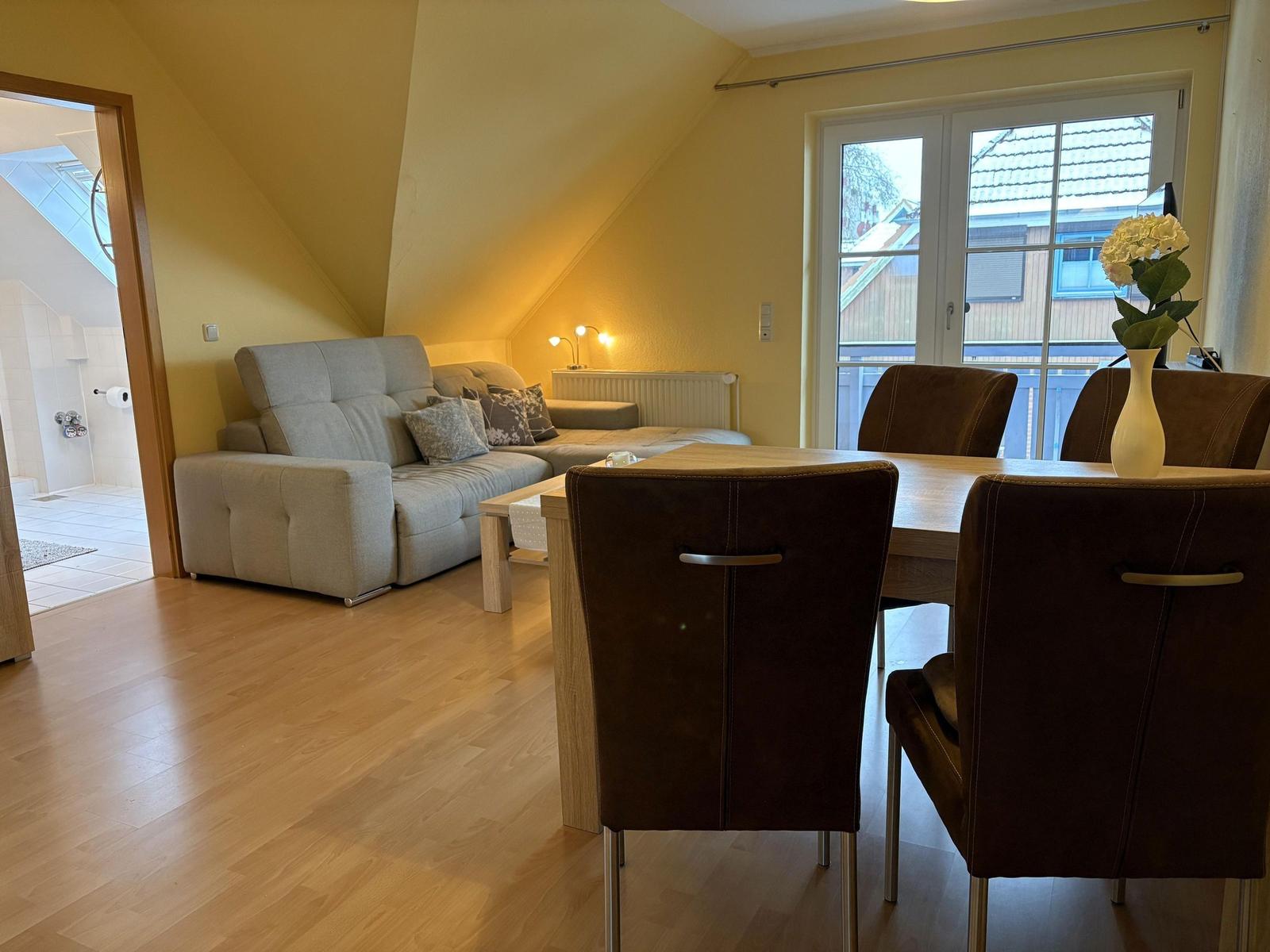 Wohn- und Essbereich mit Sofa, Tisch und Stühlen. Durchgang zur Dusche.