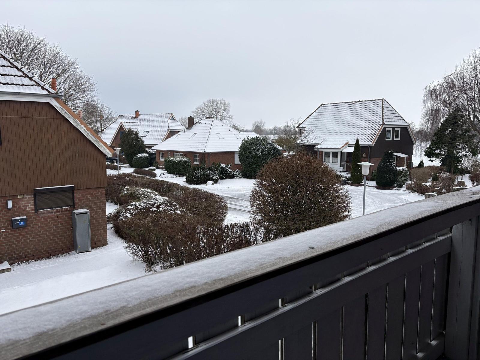 Schneebedeckte Häuser und Bäume vom Balkon aus gesehen.