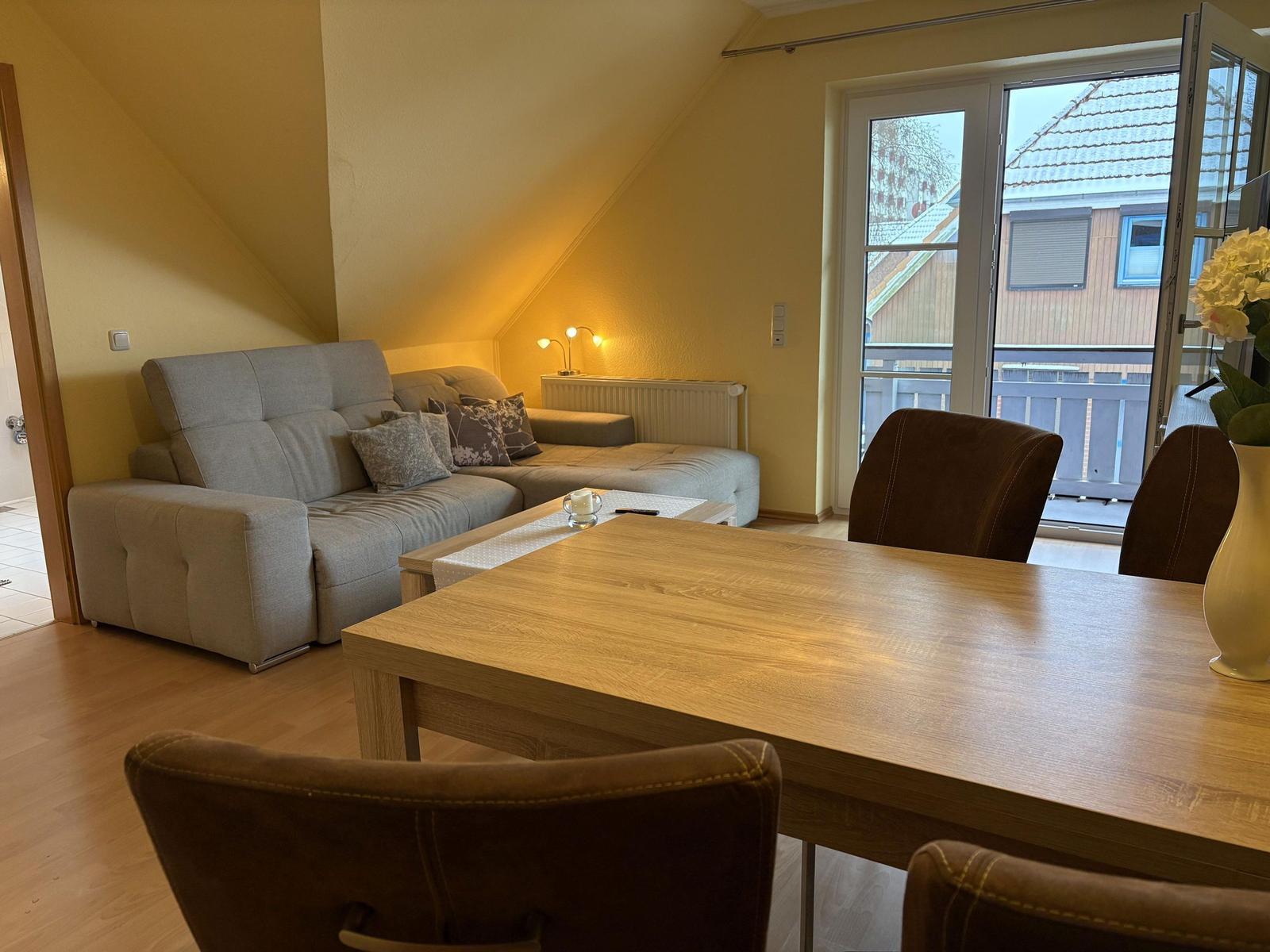 Wohn- und Essbereich mit Sofa, Tisch und Stühlen. Durchgang zur Terrasse.