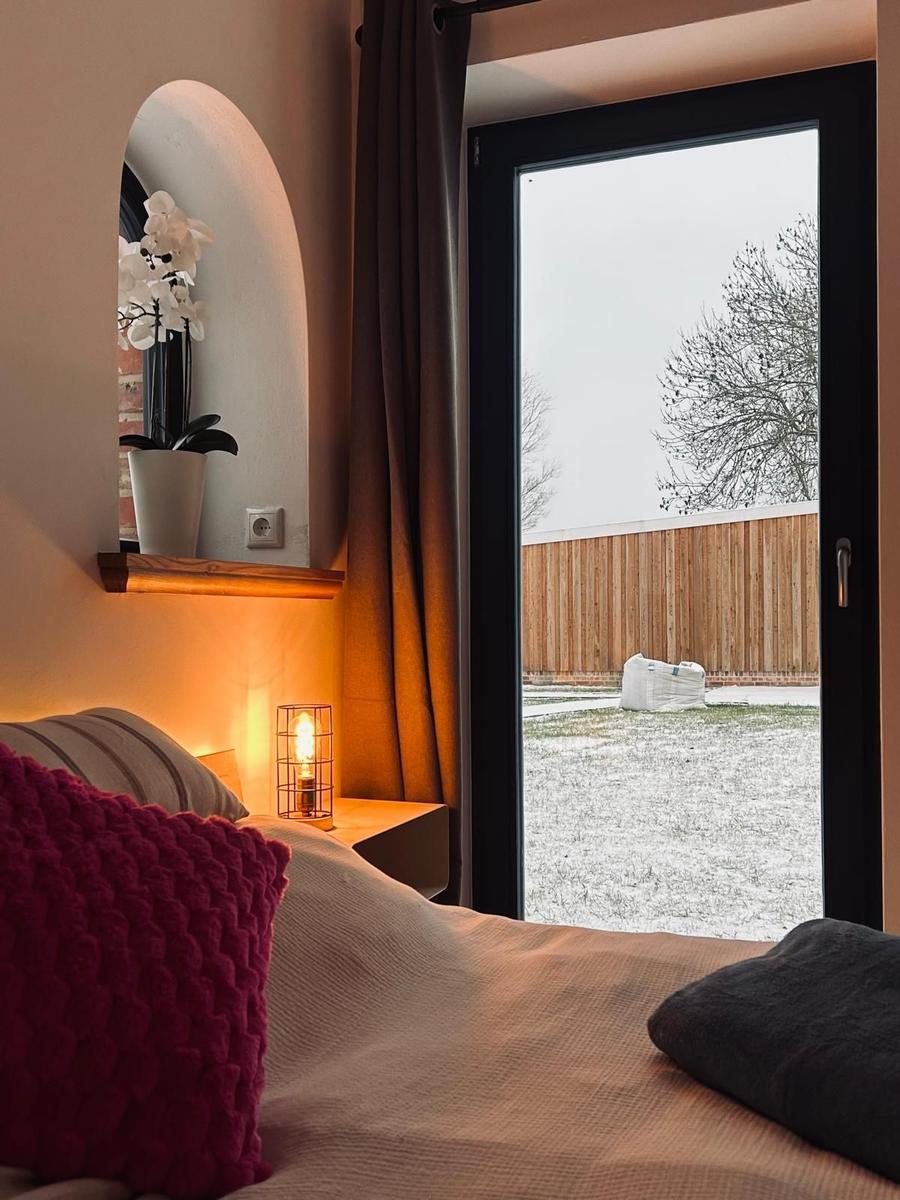 Schlafzimmer mit Blick auf verschneiten Garten. Bett, Nachttisch und Spiegel sichtbar.