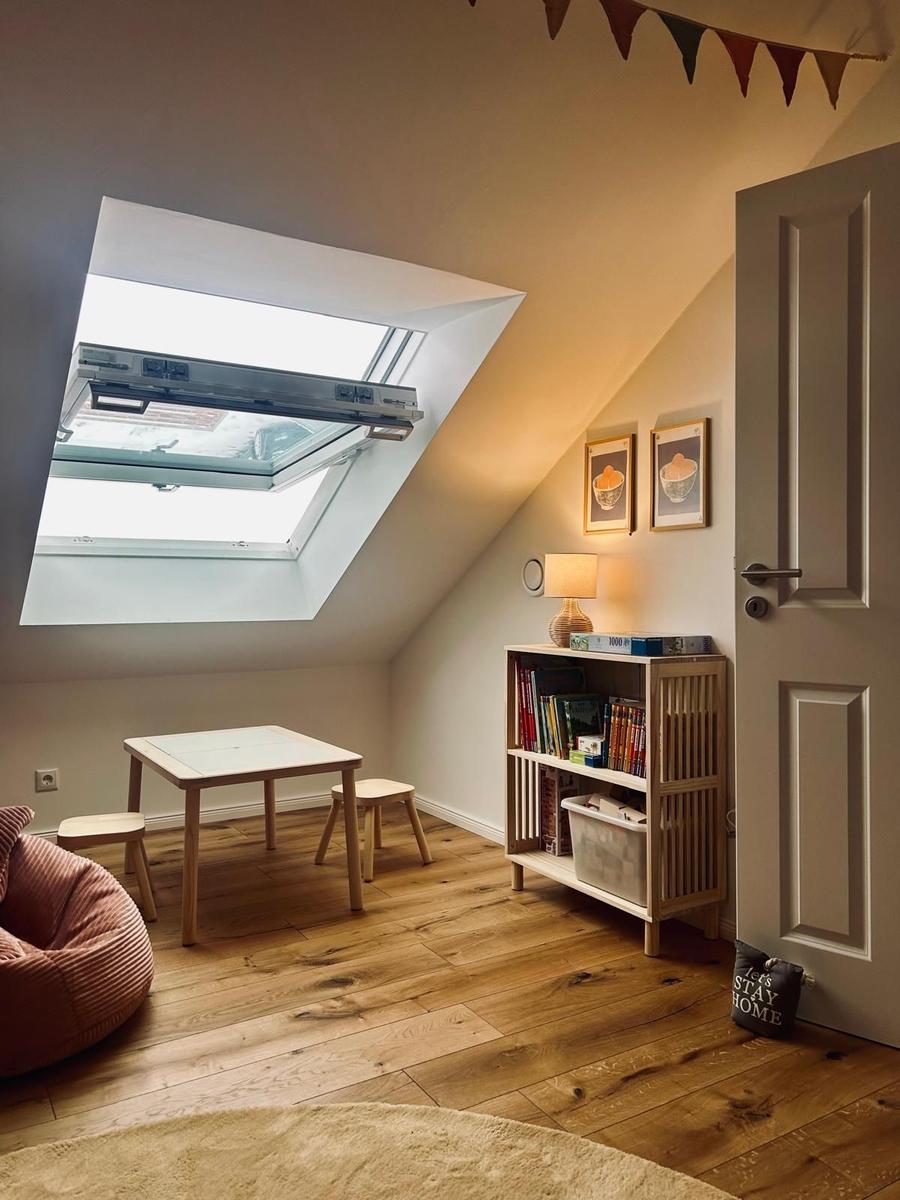 Dachgeschosszimmer mit Tisch, Stühlen, Bücherregal und Dachfenster.