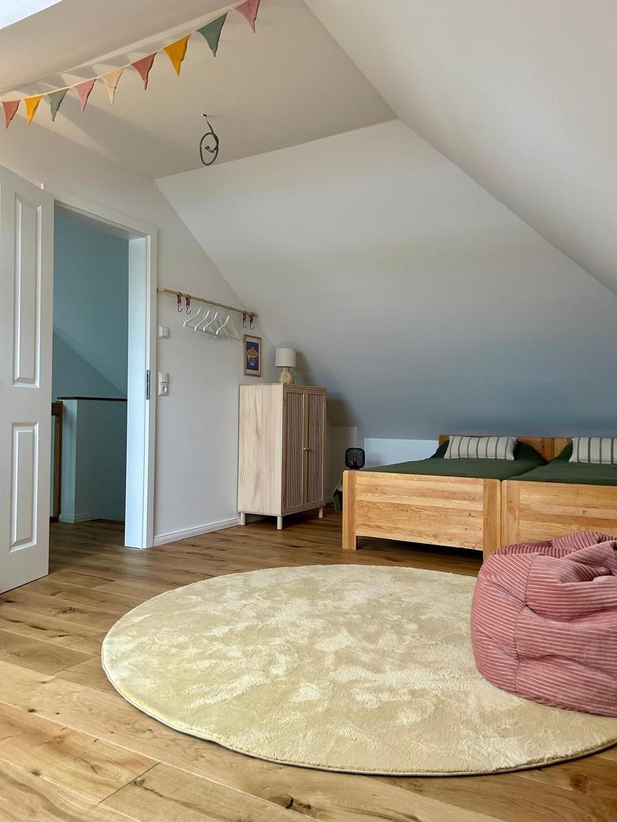 Zimmer mit Dachschrägen, Holzboden, Bett und runder Teppich.