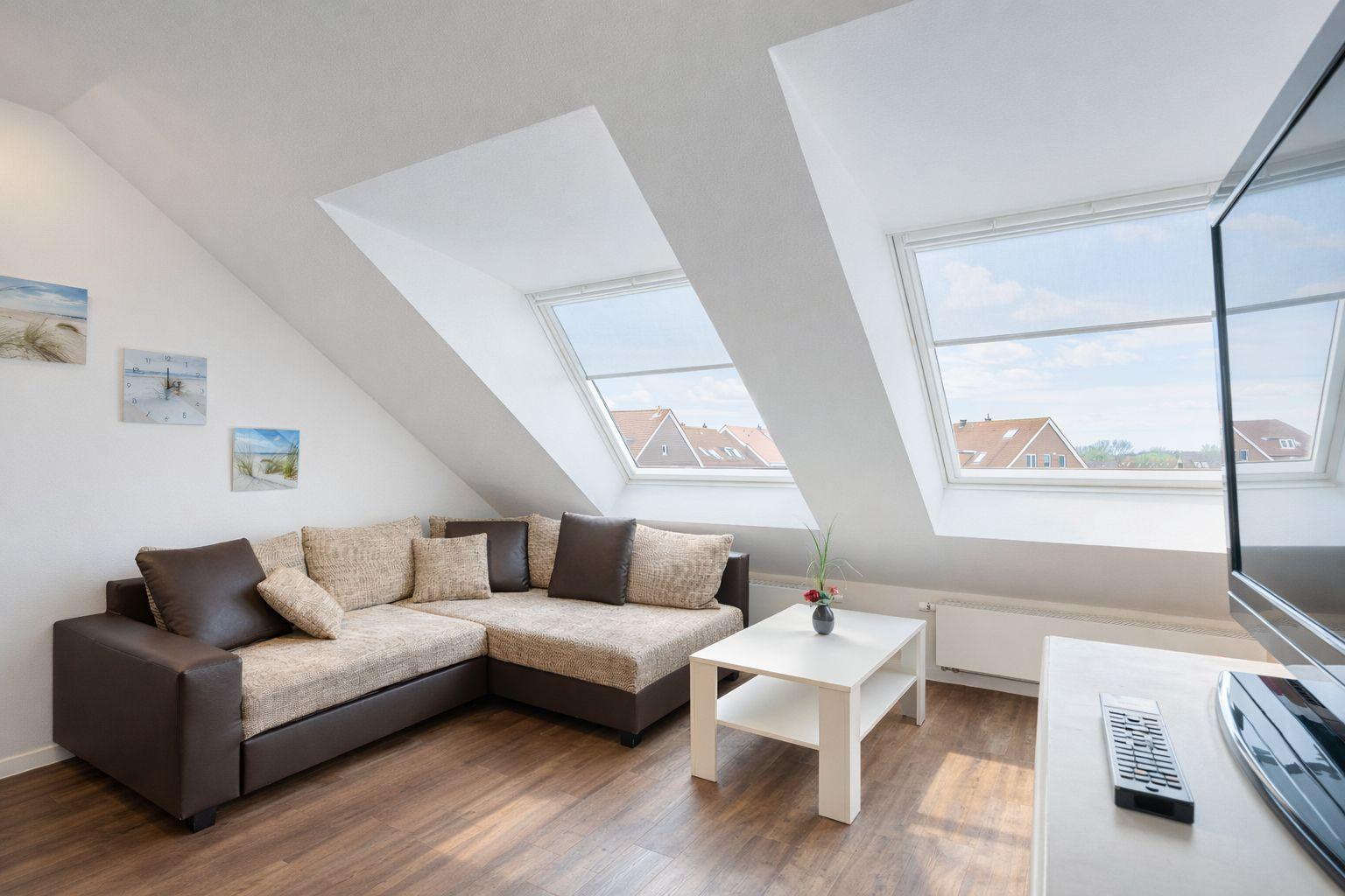 Wohnzimmer mit Ecksofa, zwei Dachfenstern und Holzboden.