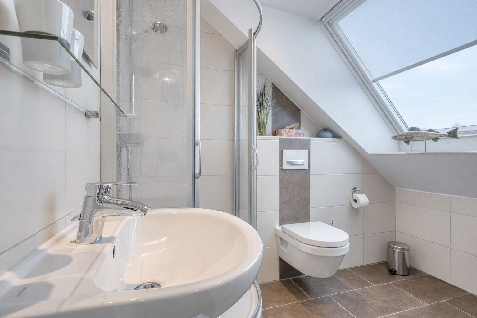 Badezimmer mit Dusche, Waschbecken und WC unter Dachschrägen mit Fenster