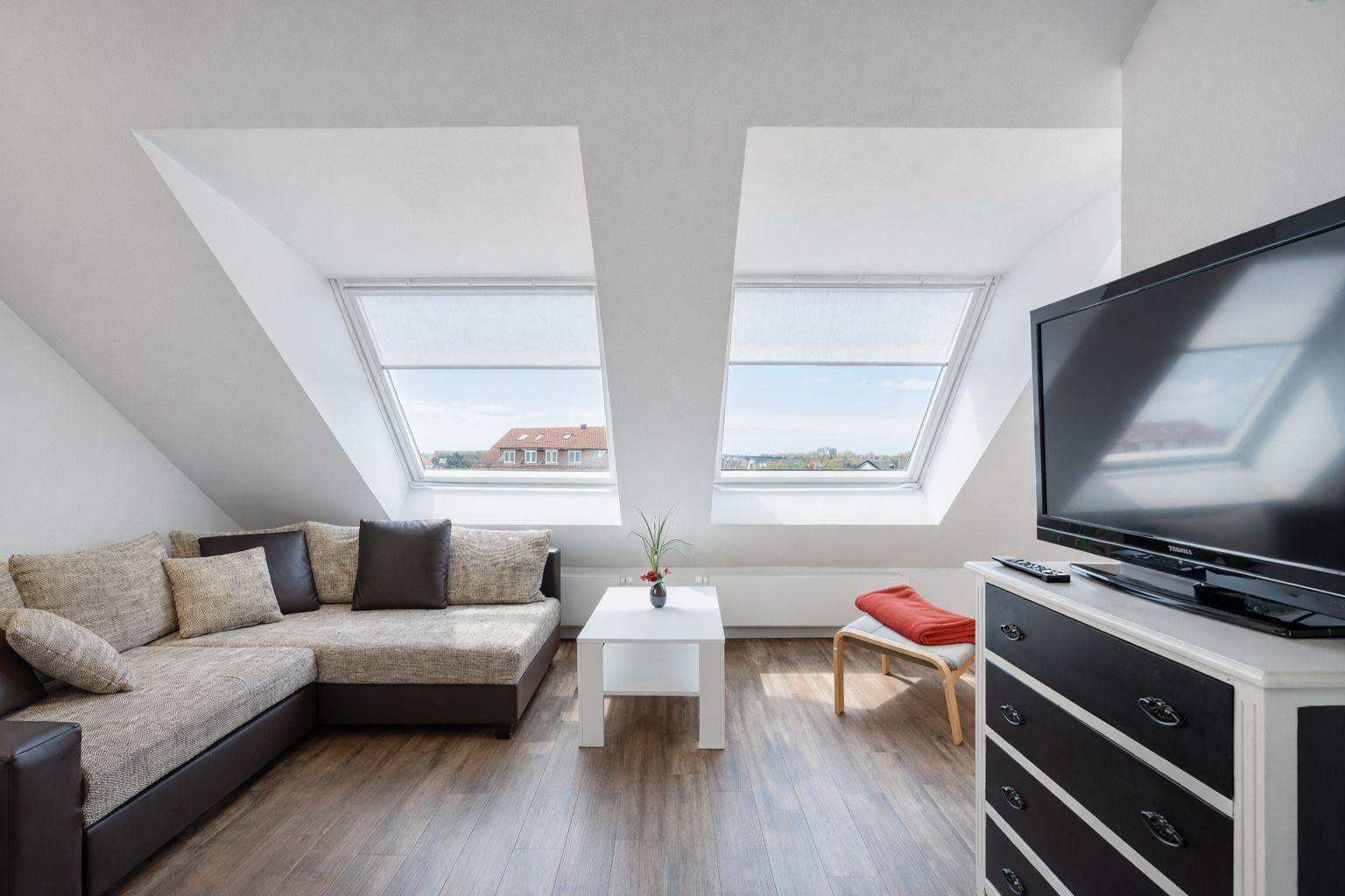 Wohnzimmer mit Dachschrägen, zwei Dachfenstern, Sofa, Couchtisch und Fernseher.