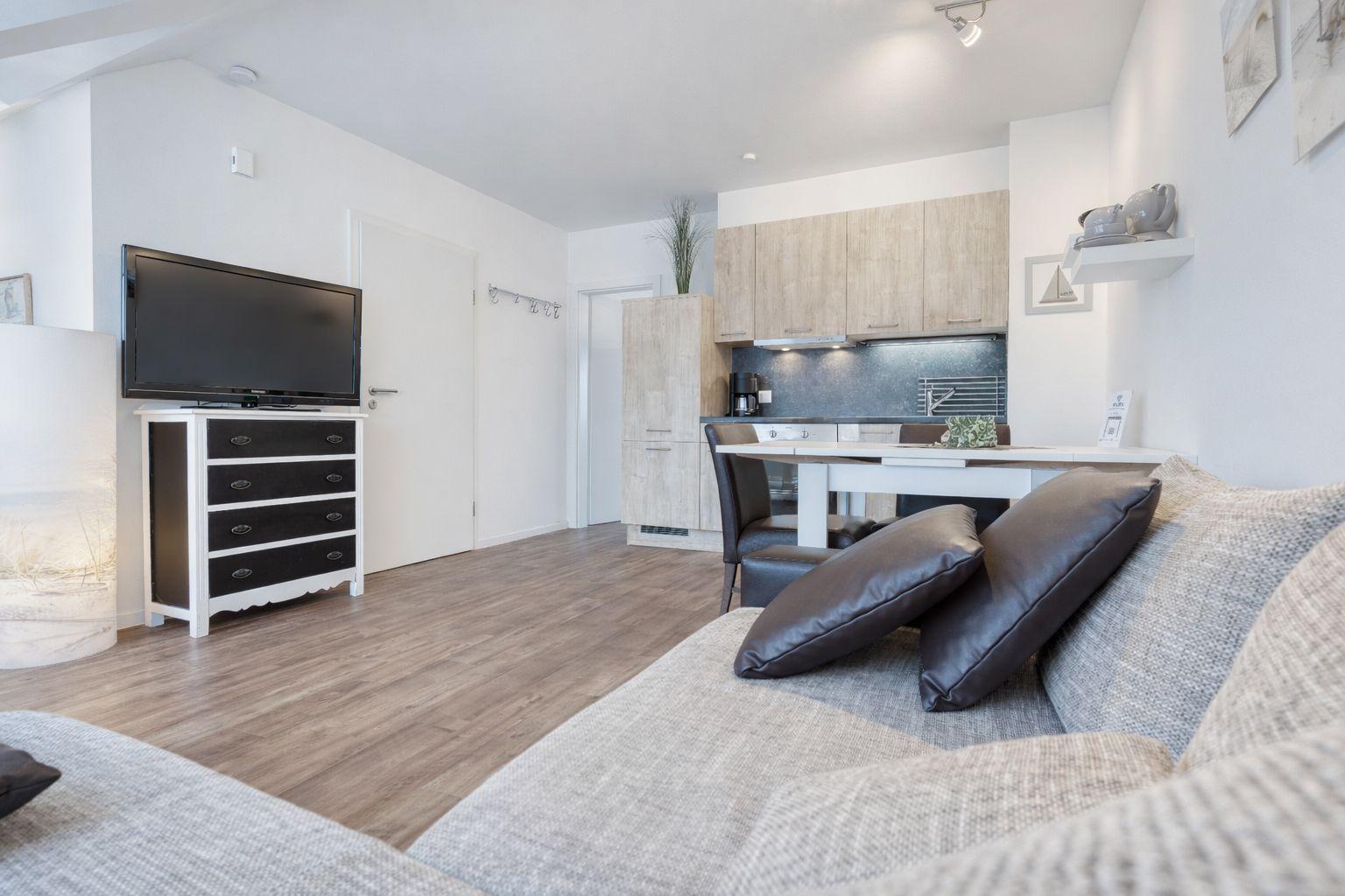 Wohn- und Küchenbereich mit Sofa, Fernseher und Holzboden.