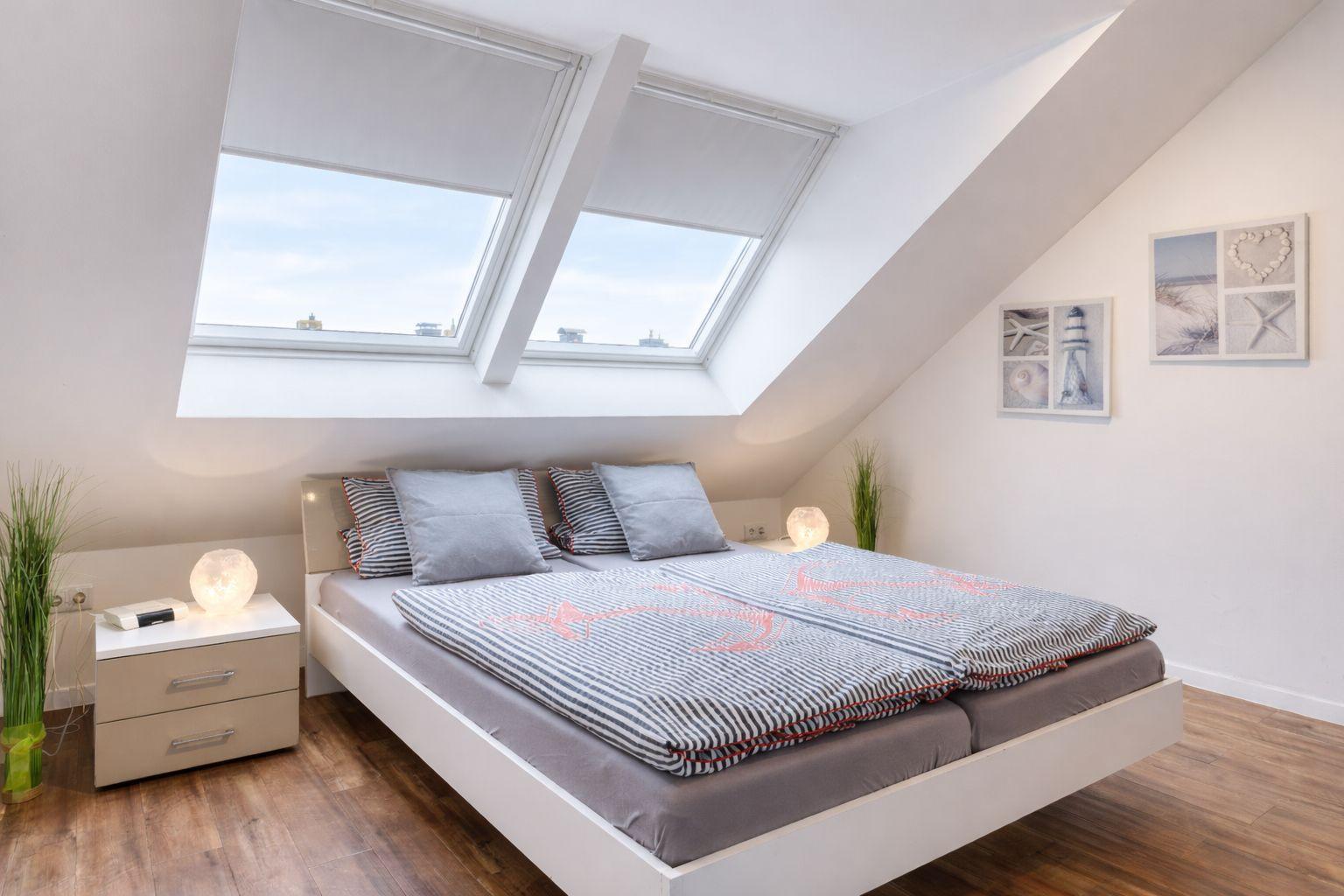 Schlafzimmer mit Dachschrägen, Doppelfenster und Bett mit Bettwäsche.