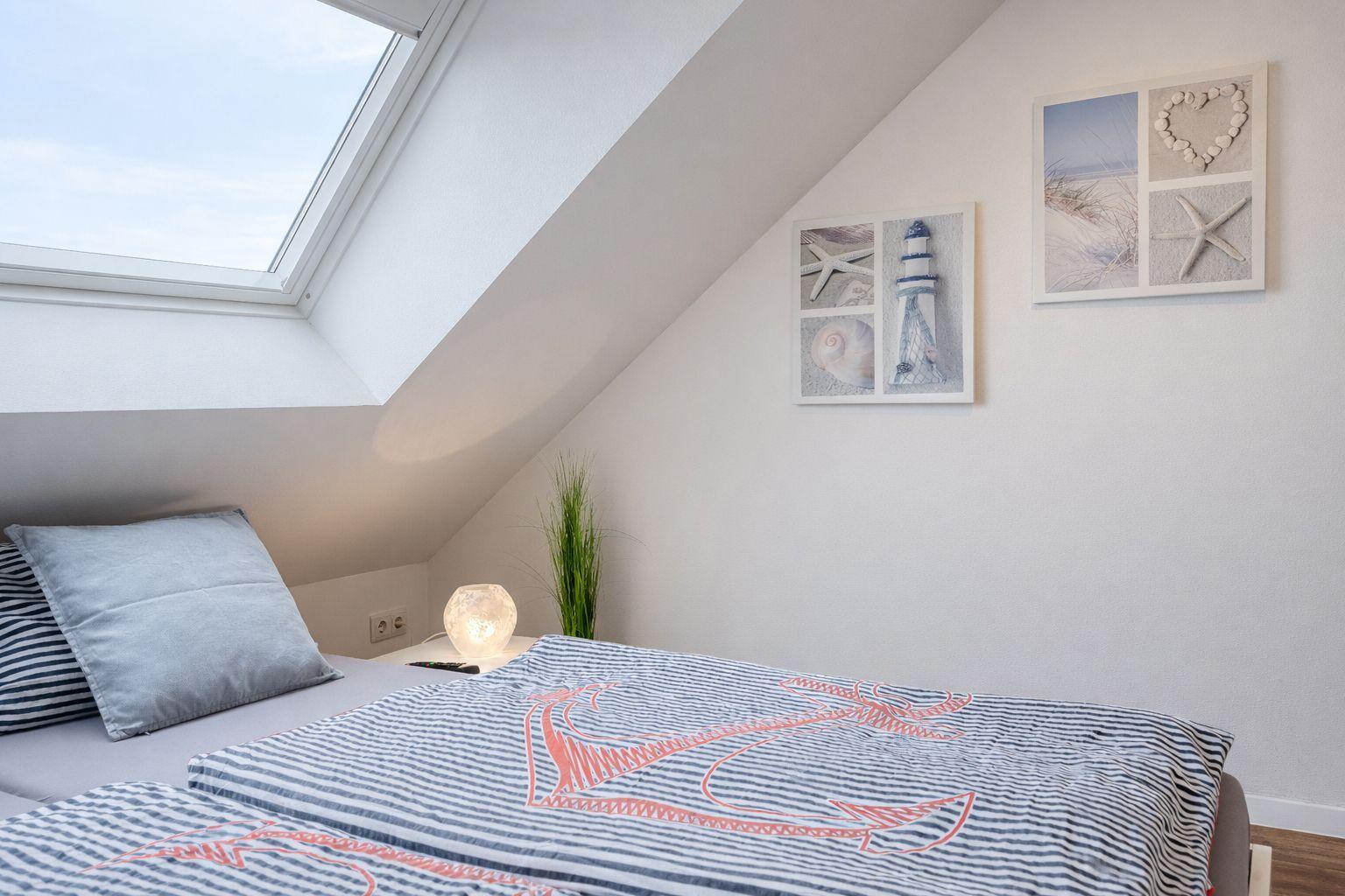 Schlafzimmer mit Dachschrägen, Dachfenster und Strandmotiven an den Wänden.