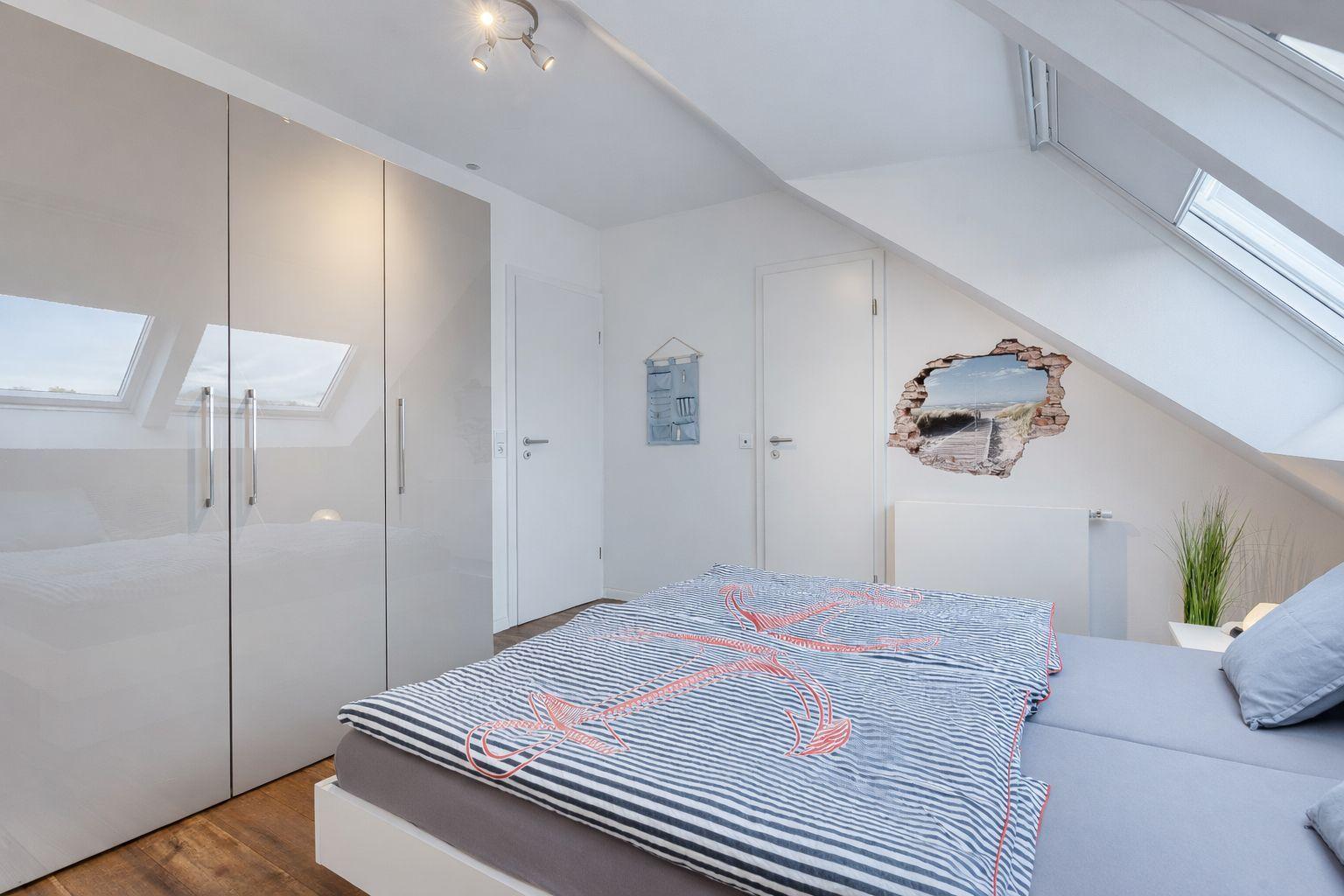 Schlafzimmer mit Dachschrägen, großem Bett und Schwebetüren. Wanddekoration mit Strandmotiv.