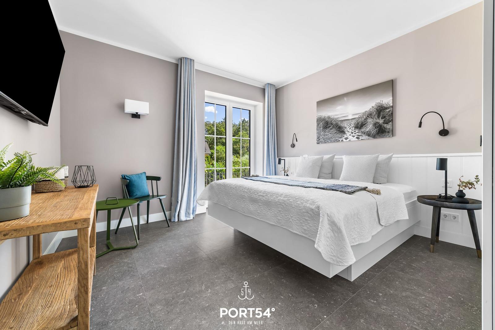 Schlafzimmer mit Bett, TV, Tisch und Fenster zur Außenseite.