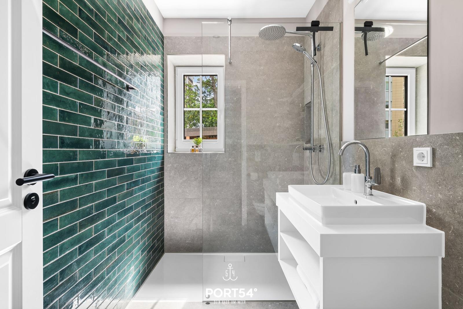 Badezimmer mit Dusche, Waschbecken und grünen Fliesen.