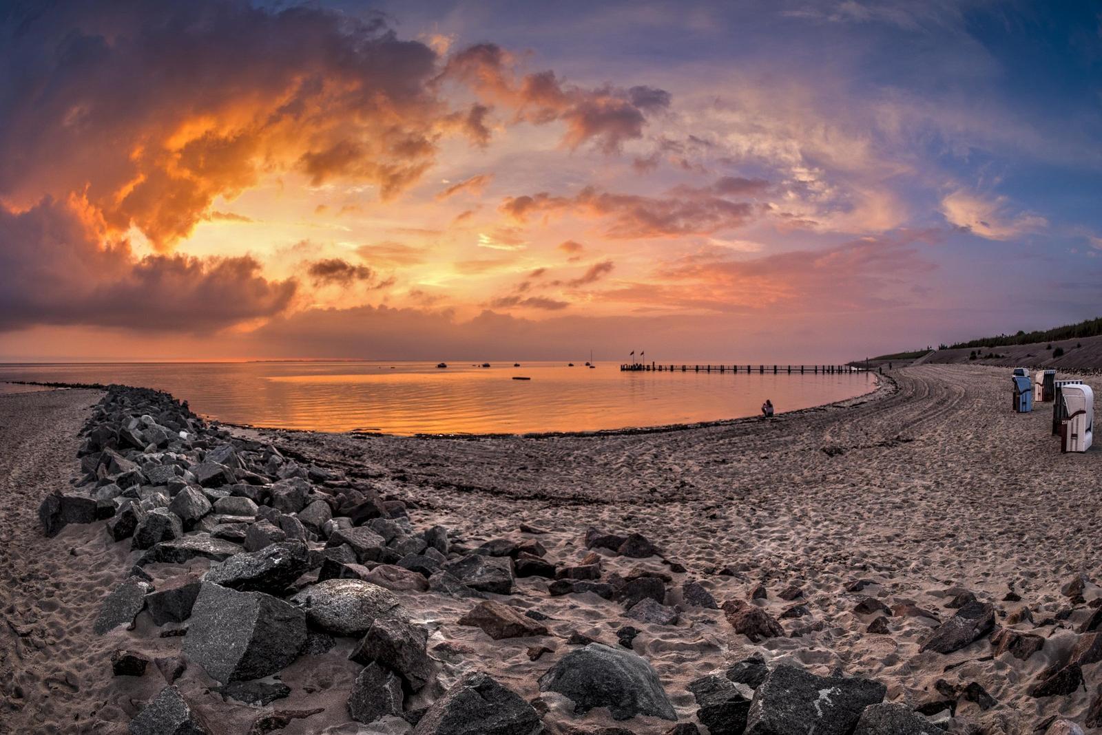 Strand bei Sonnenuntergang mit Steinschutz und Strandkörben.