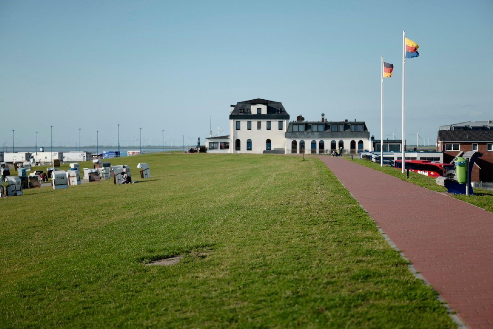 Weite Grünfläche mit Strandkörben, Weg und Gebäude im Hintergrund.