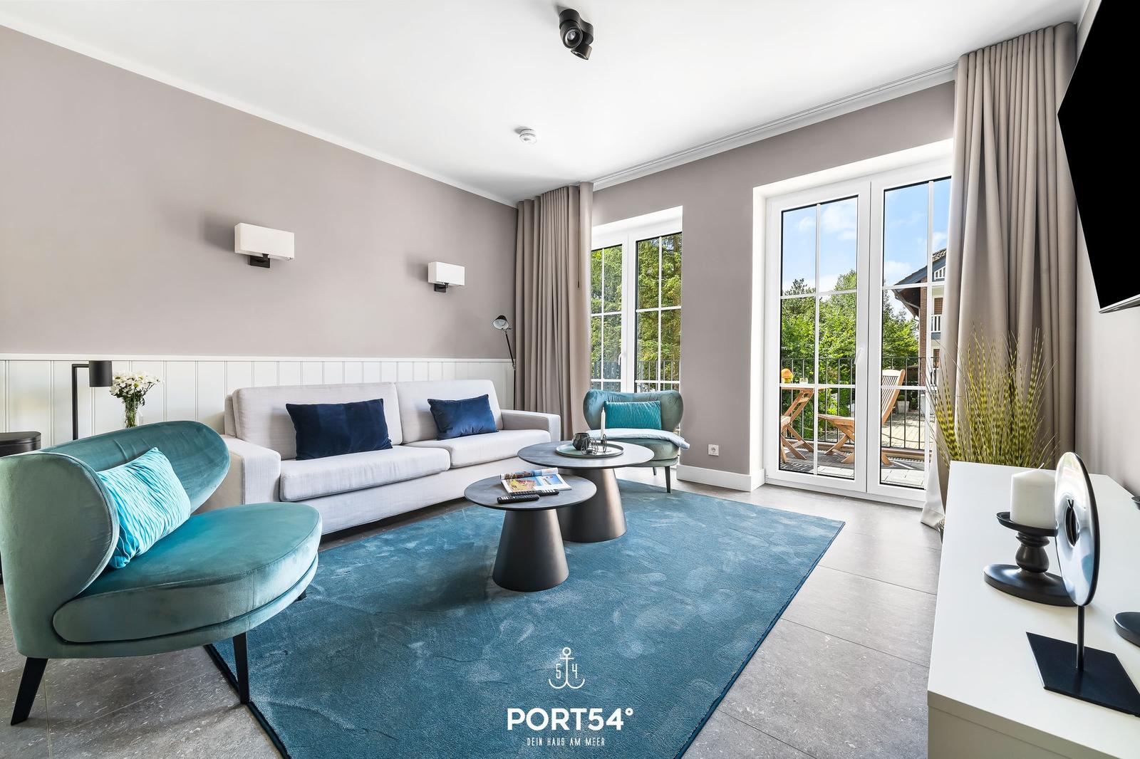 Wohnzimmer mit Sofa, Sesseln und Terrasse. Blauer Teppich und Holzboden.