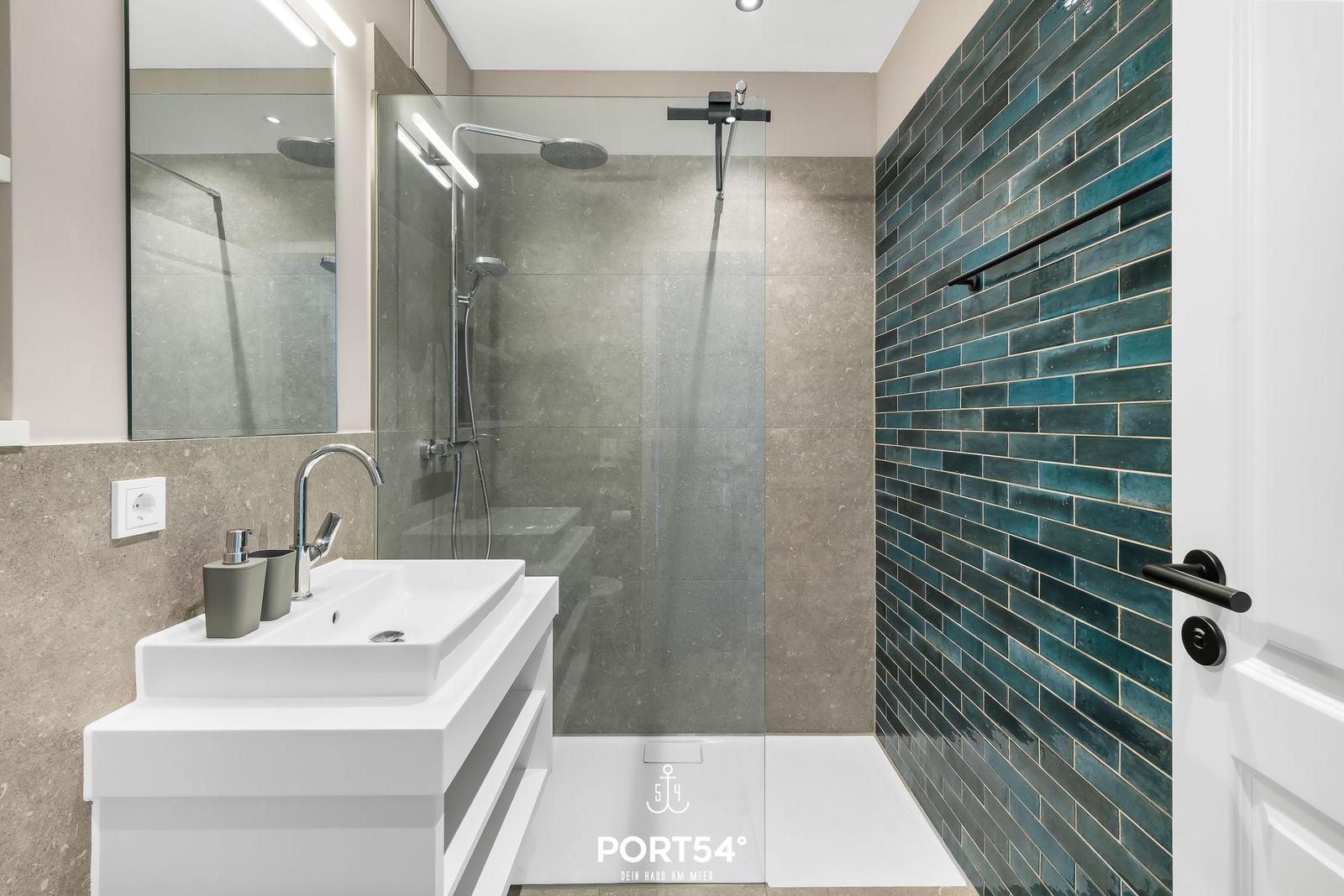 Badezimmer mit Dusche, Waschbecken und blauen Fliesen.