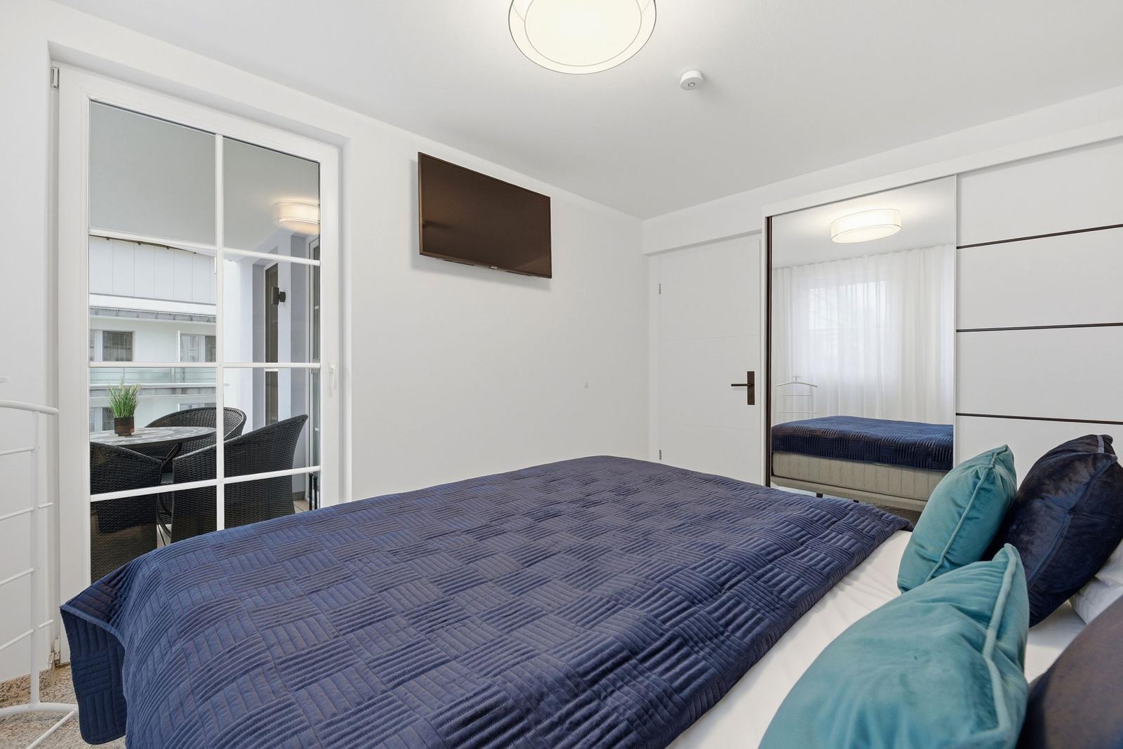 Schlafzimmer mit Bett, TV und Balkonzugang.