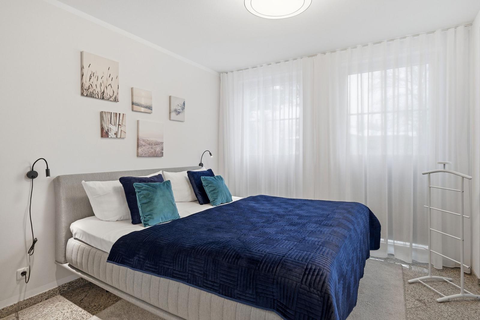 Schlafzimmer mit Bett, Vorhängen und Wandbildern.