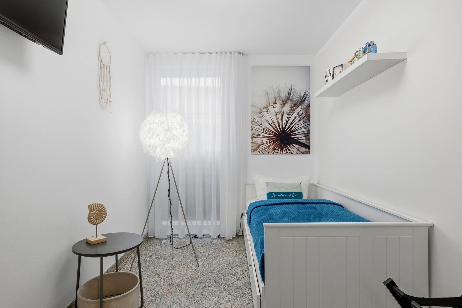 Schlafzimmer mit Bett, Fenster, Stehlampe und Wandbild.