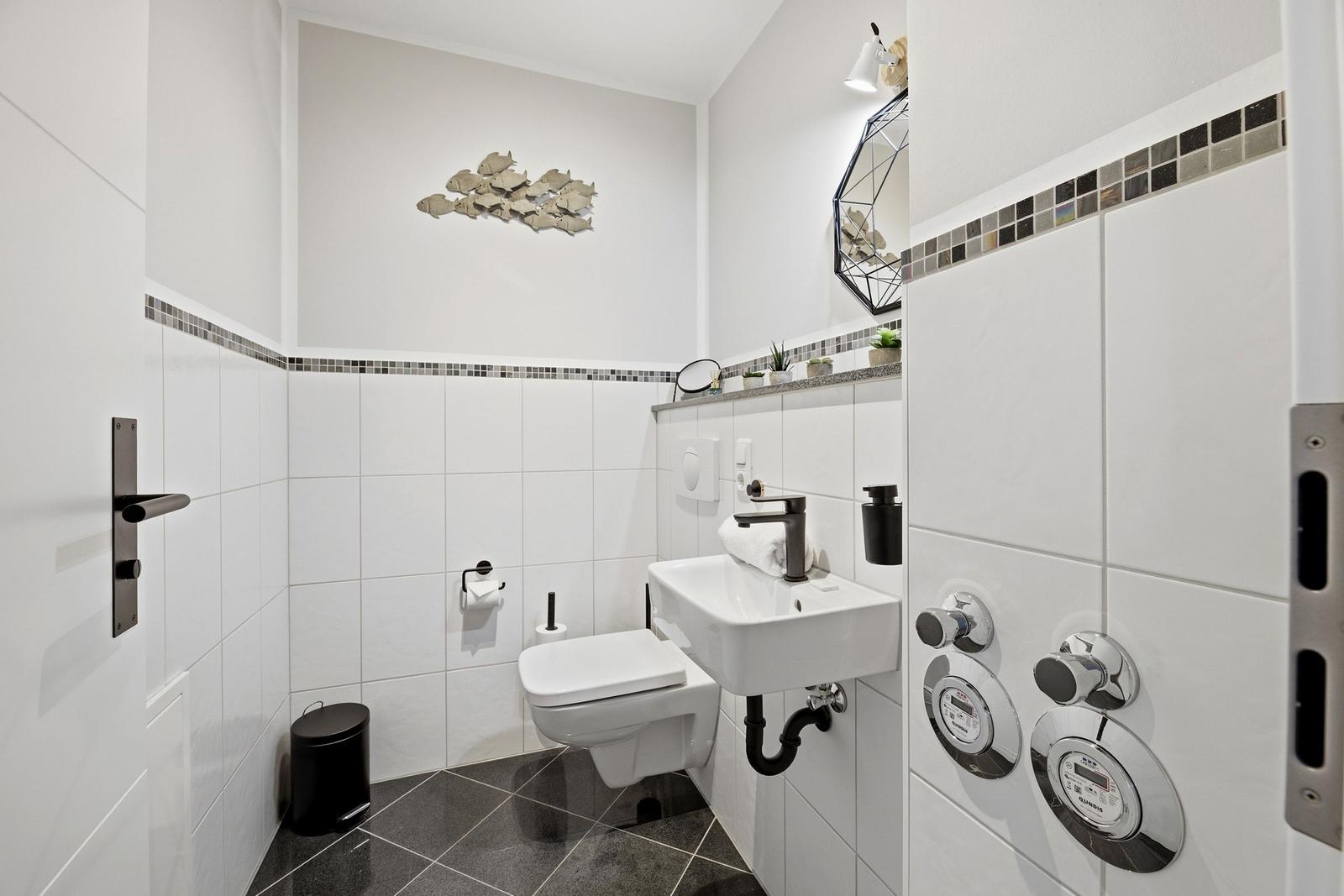 Badezimmer mit Toilette, Waschbecken und Dusche. Wanddekoration und Mosaikfliesen.
