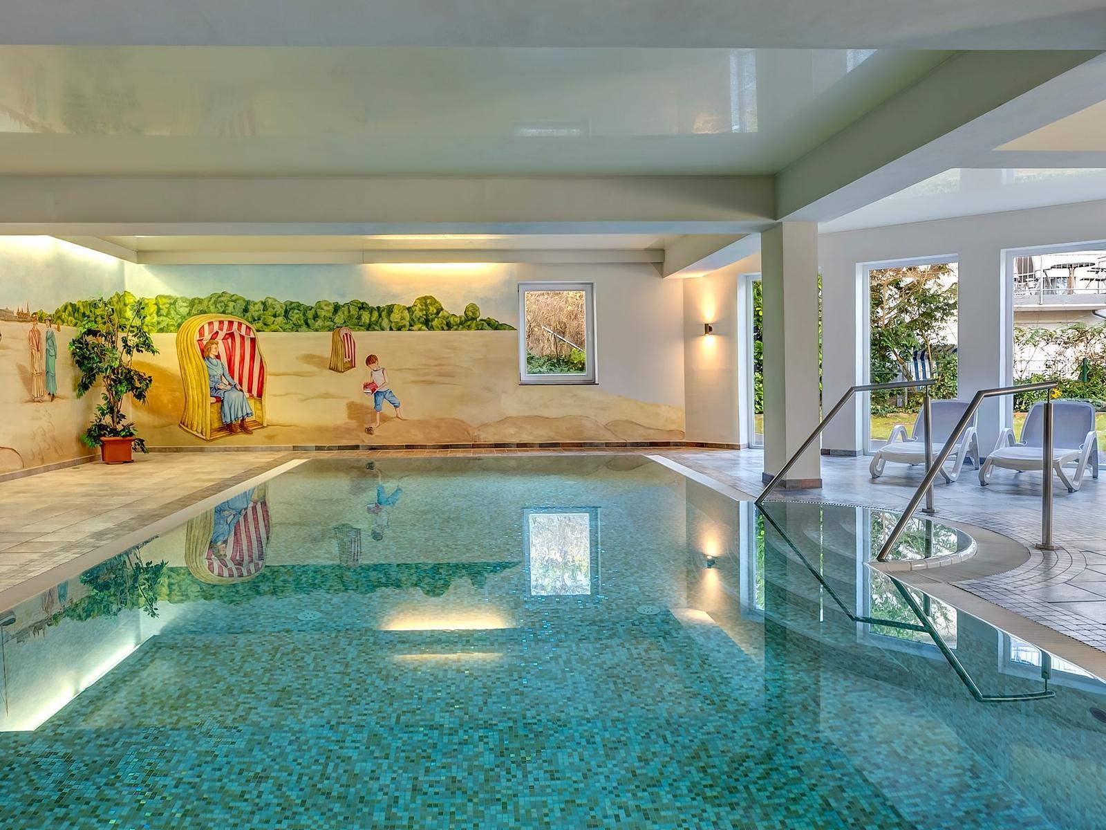 Innenpool mit Wandmalerei und Außenterrasse mit Liegestühlen.