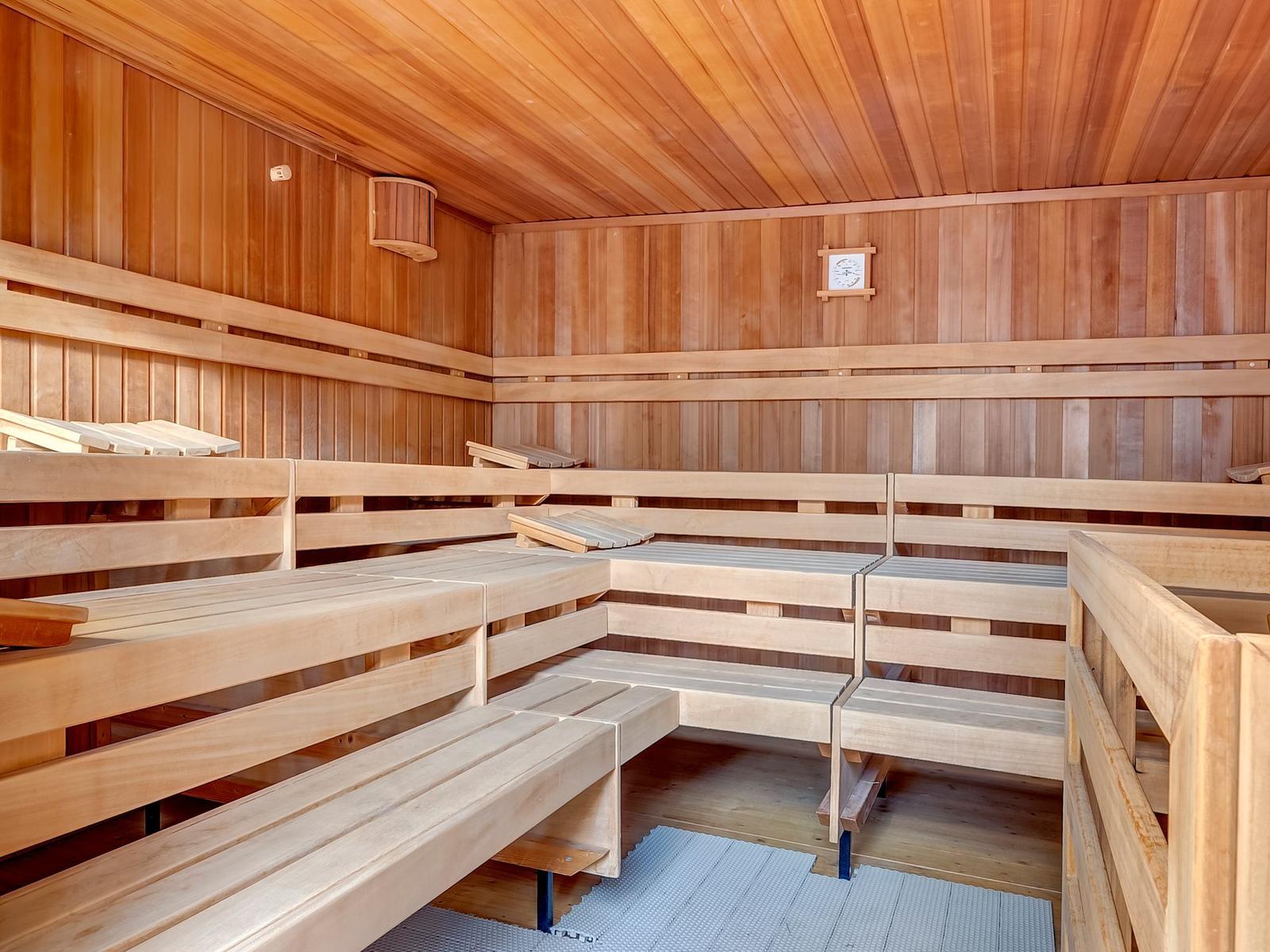 Holzsauna mit mehreren Sitzbänken und Temperaturanzeige an der Wand.