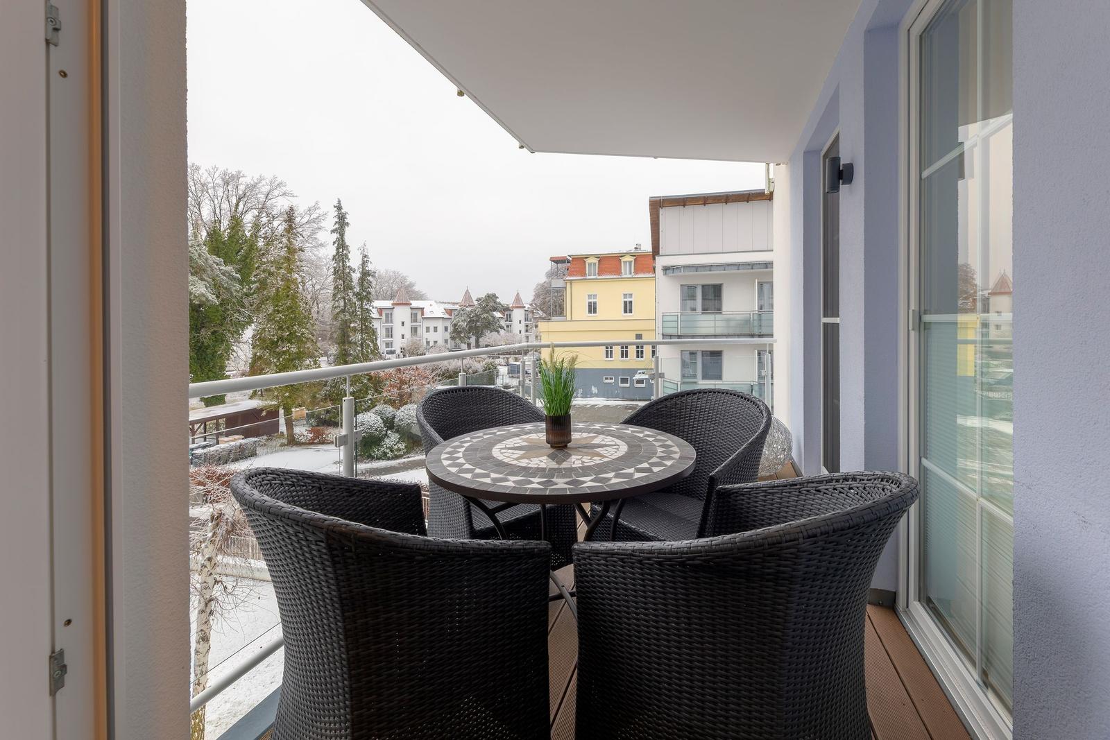 Terrasse mit Tisch und Stühlen, Blick auf schneebedeckte Bäume und Gebäude.