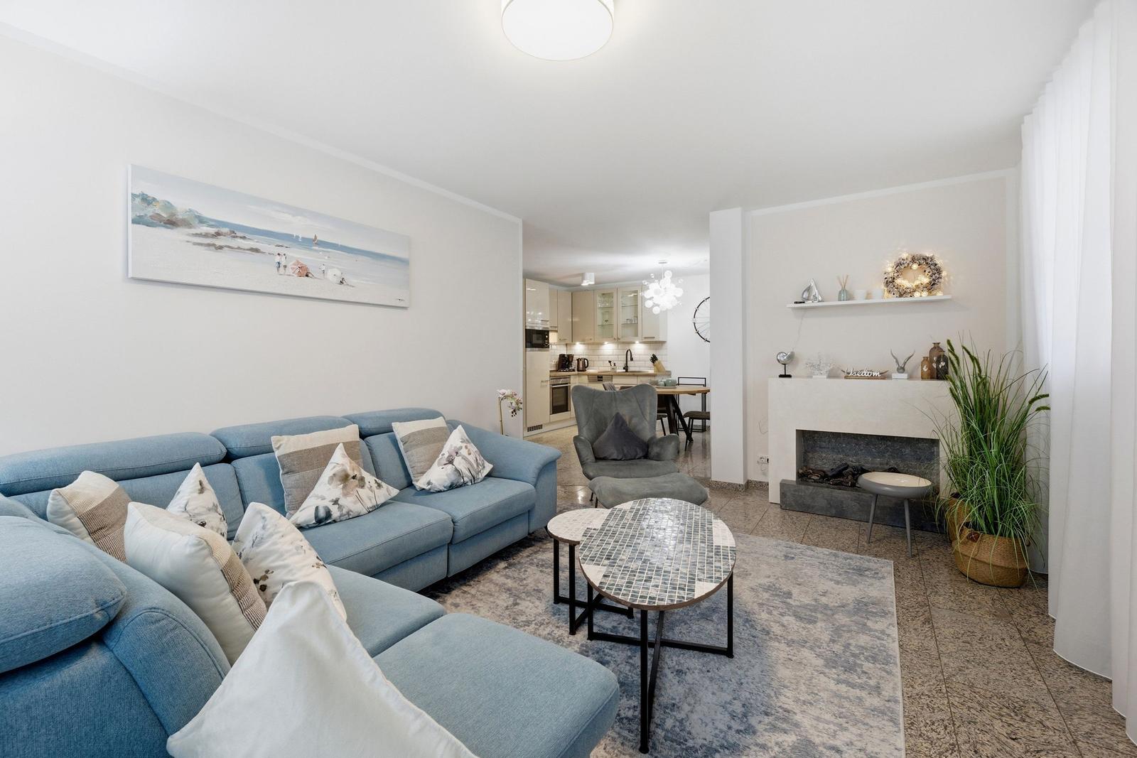 Wohnzimmer mit Sofa, Kamin und Blick in die Küche.