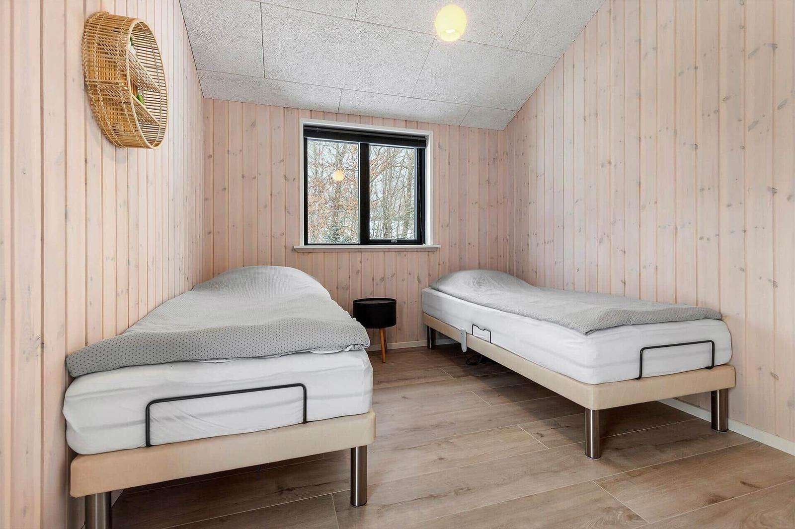 Zwei Einzelbetten in einem Raum mit Holzwänden und Fenster.