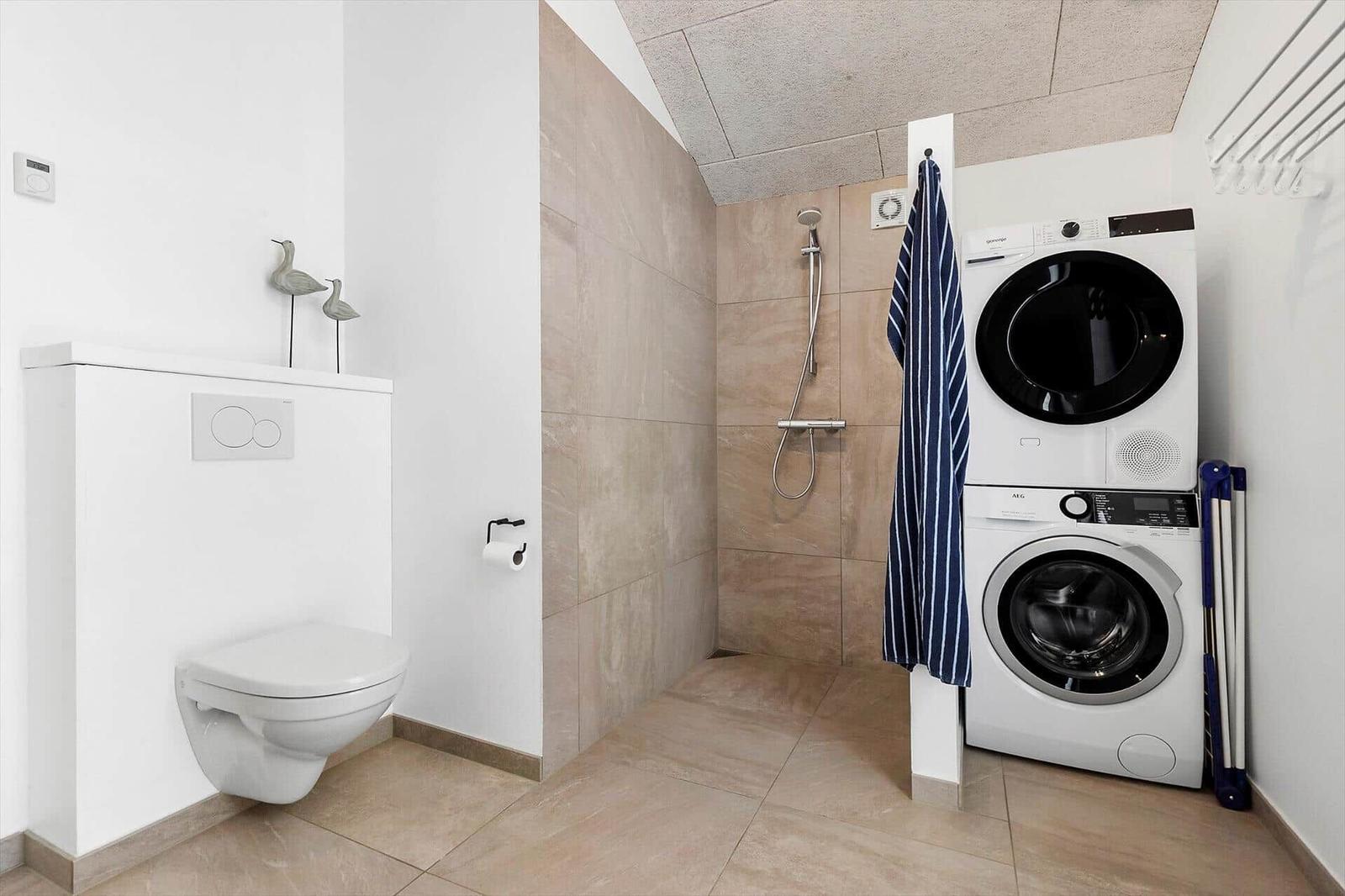 Badezimmer mit Dusche, Toilette und Waschmaschine-Trockner-Kombination.