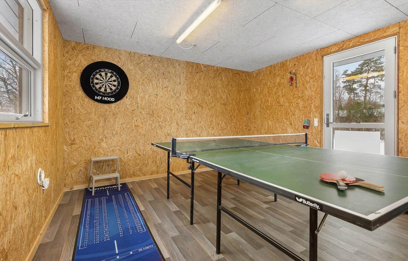 Raum mit Tischtennisplatte, Dartboard und Fenster. Holzwand und Boden.