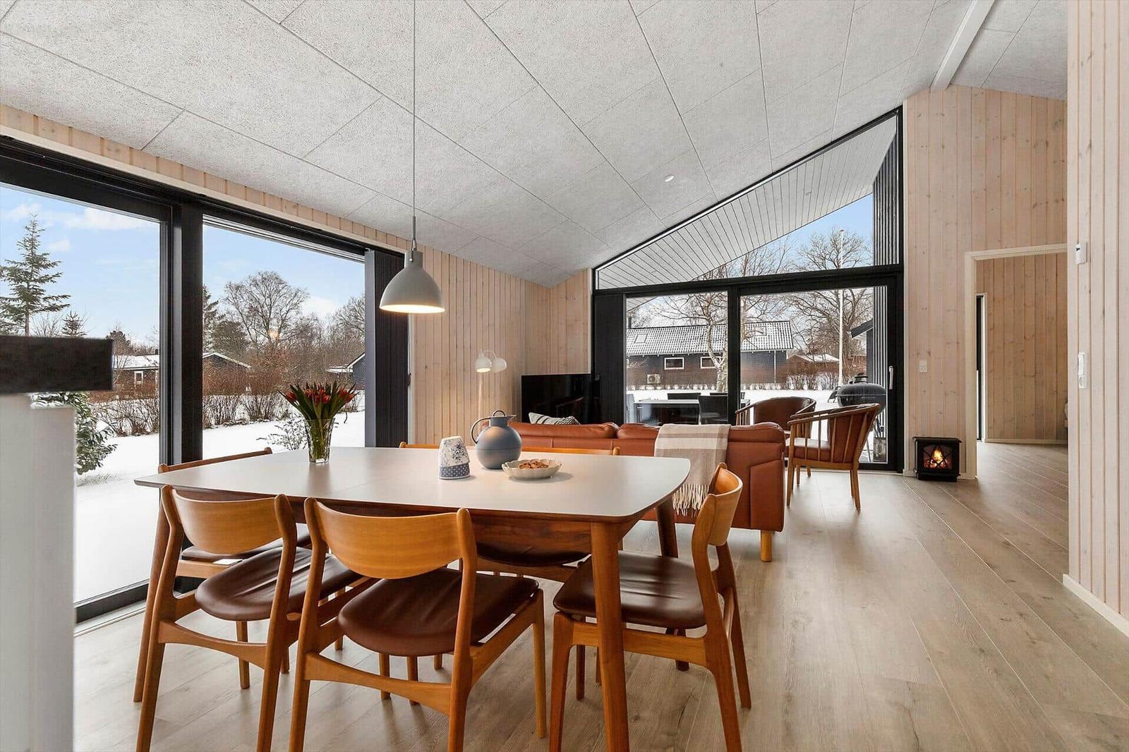 Essbereich mit Tisch und Stühlen, großflächige Fenster, Holzwände und Sitzbereich im Hintergrund.