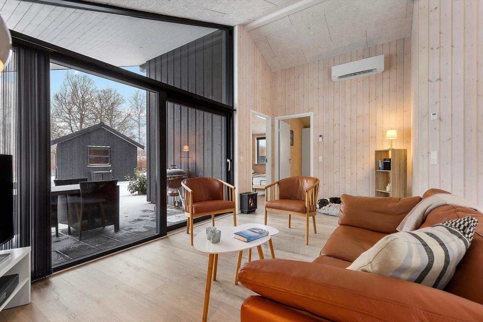 Wohnzimmer mit braunen Ledermöbeln, Holzwand und großem Fenster zur Terrasse.
