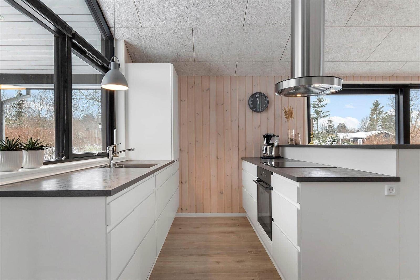Moderne Küche mit weißen Schränken, Holzwand und großem Fenster. Edelstahl-Abluft und Kaffeemaschine.