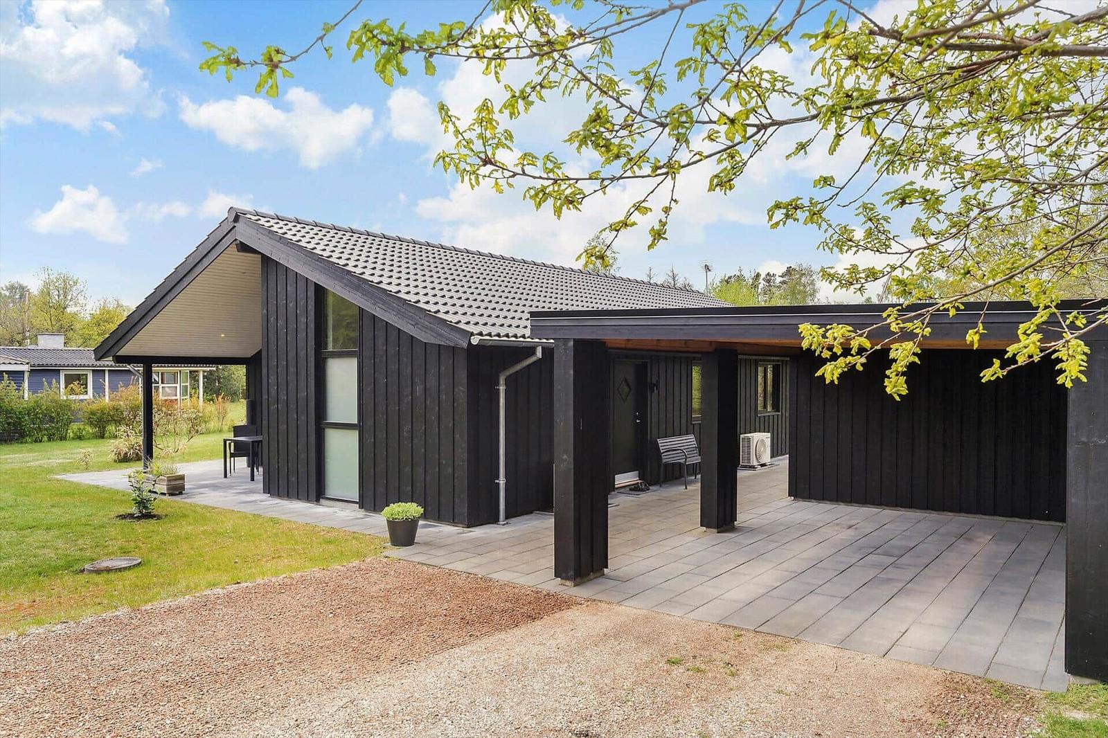 Moderne Holzhütte mit Terrasse und Garten unter blauem Himmel.