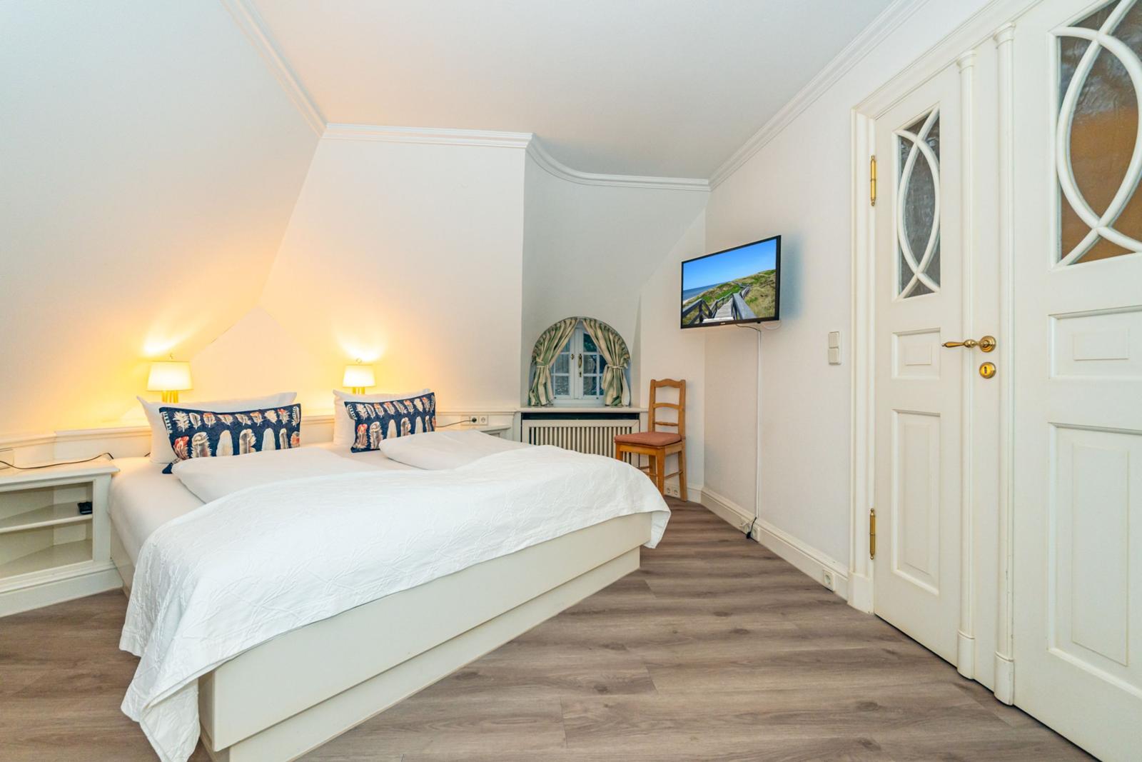 Schlafzimmer mit Doppelbett, Fernseher und Holzboden.