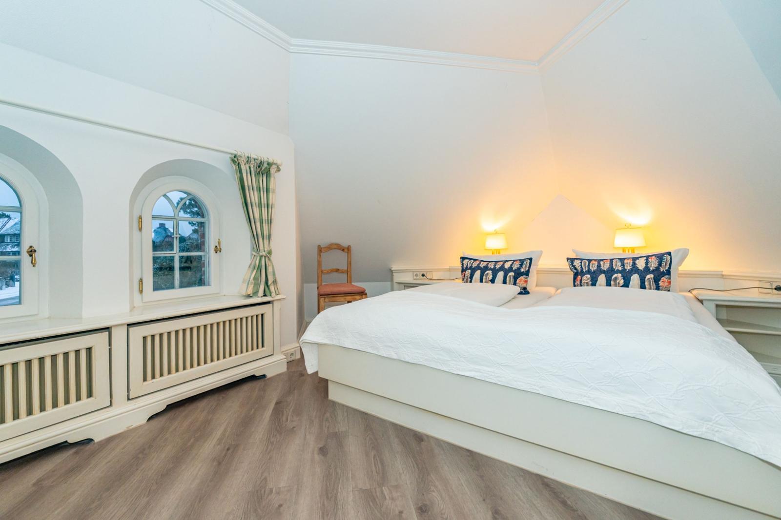 Schlafzimmer mit Doppelbett, zwei Fenstern und Holzboden.