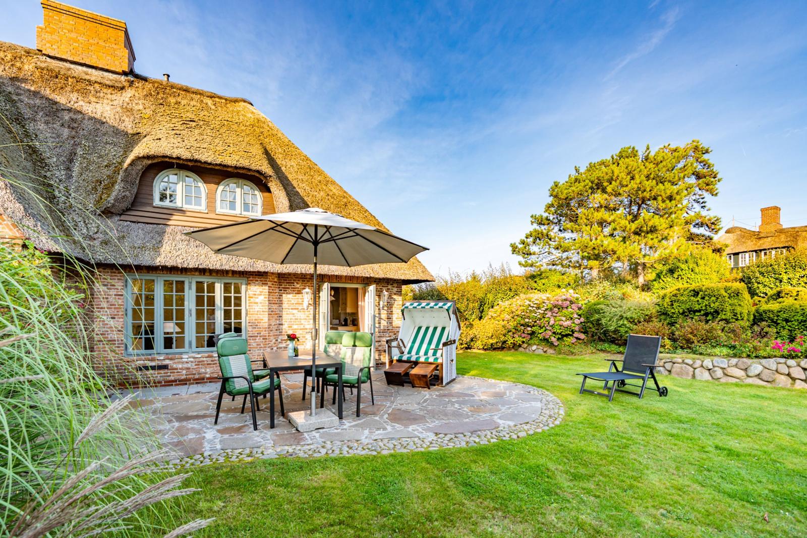 Haus mit Strohdach, Garten mit Tisch, Stühlen und Liege