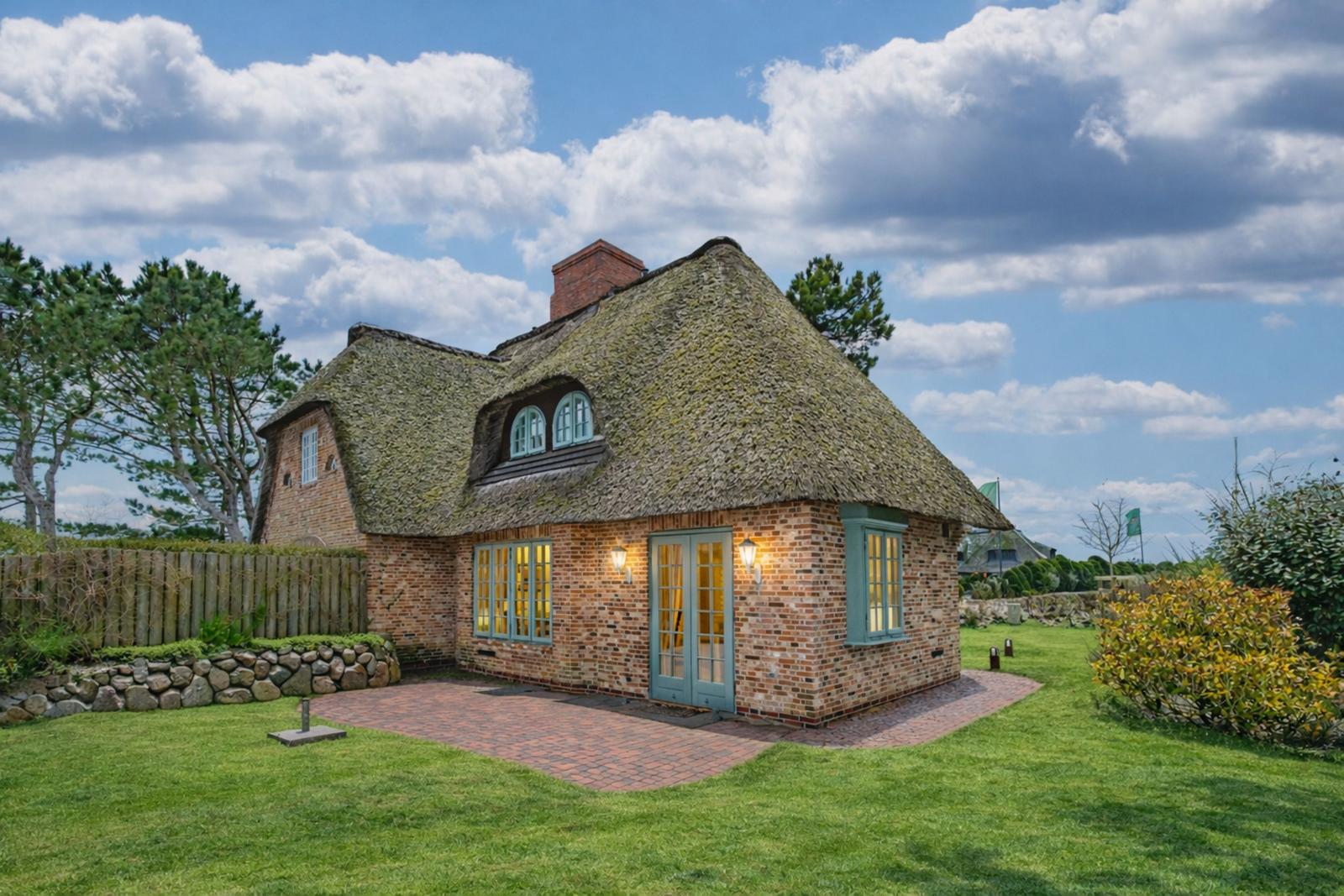 Haus mit Strohdach, Backsteinfassade und grünen Fensterrahmen auf grünem Rasen.