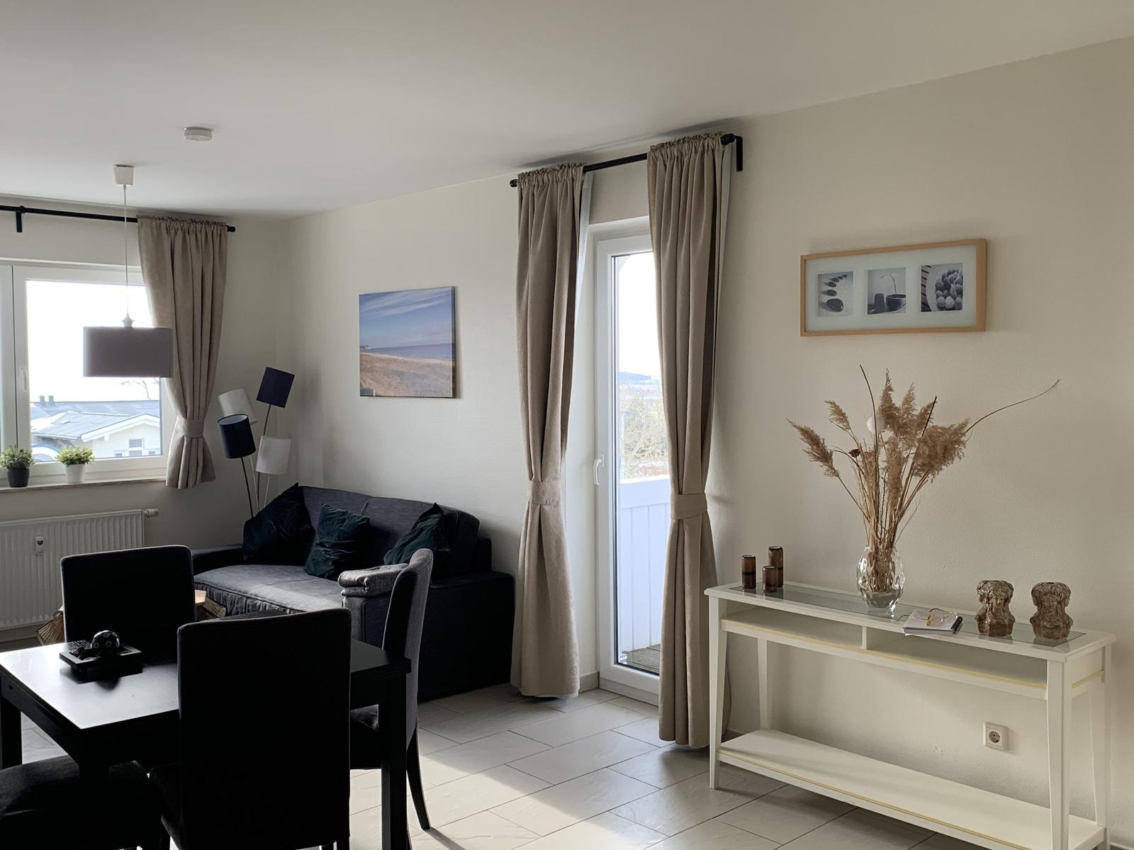 Wohnzimmer mit Sofa, Esstisch und Balkontür. Wandbild und Konsole mit Dekoration.