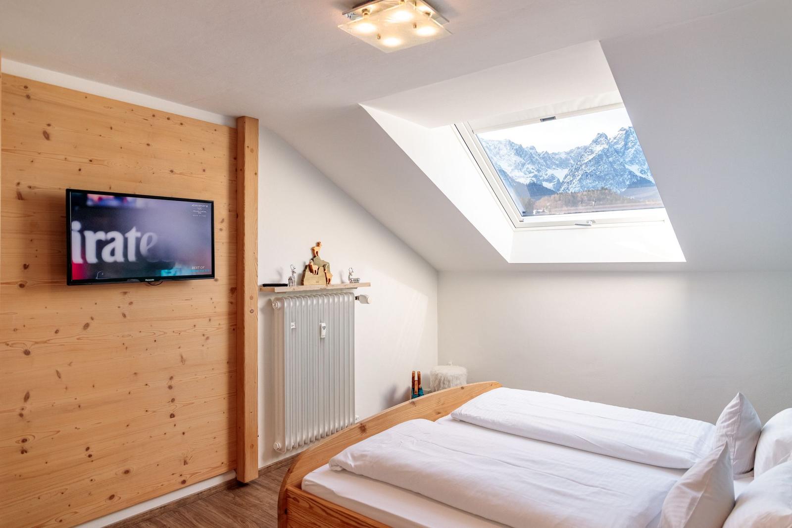 Schlafzimmer mit Dachfenster und TV an Holzwand.