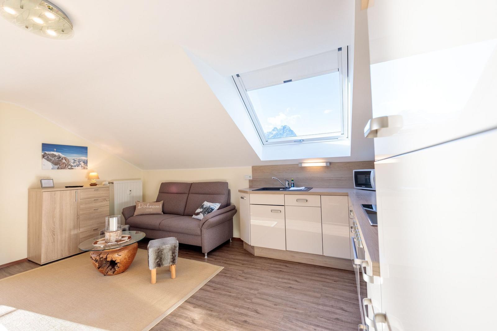 Wohnbereich mit Sofa, Küchenzeile und Dachfenster mit Bergblick.