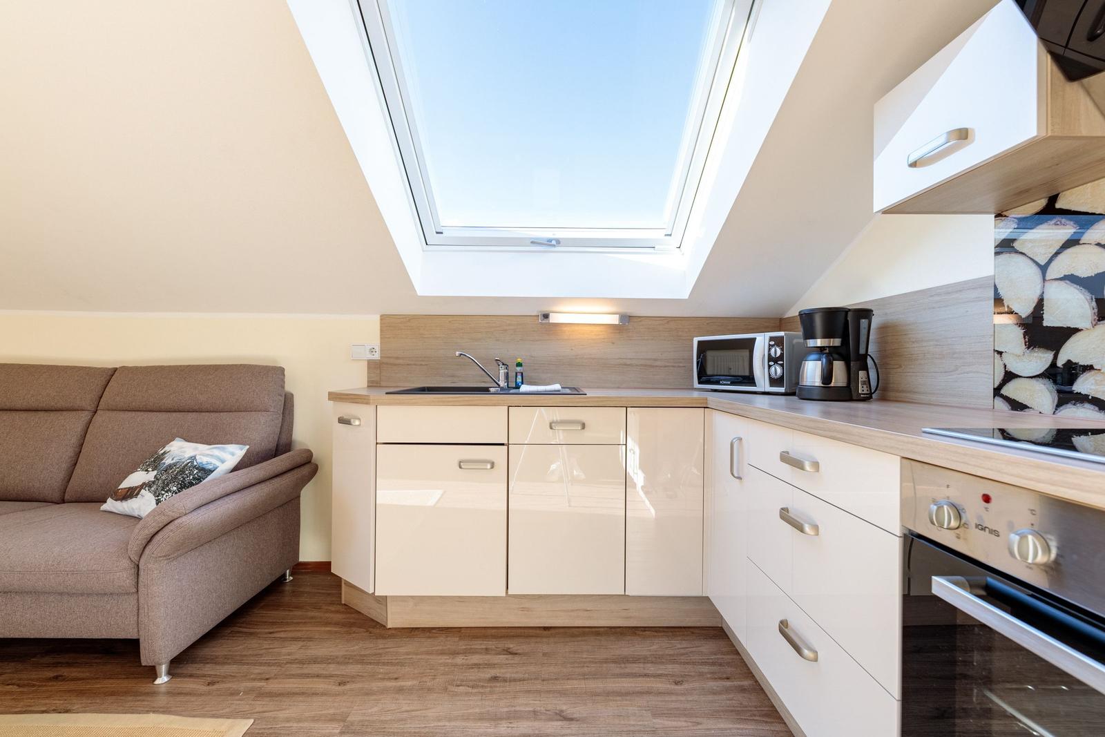Küche mit Sofa, Dunstabzug und Dachfenster. Arbeitsplatte und Schränke sind sichtbar.