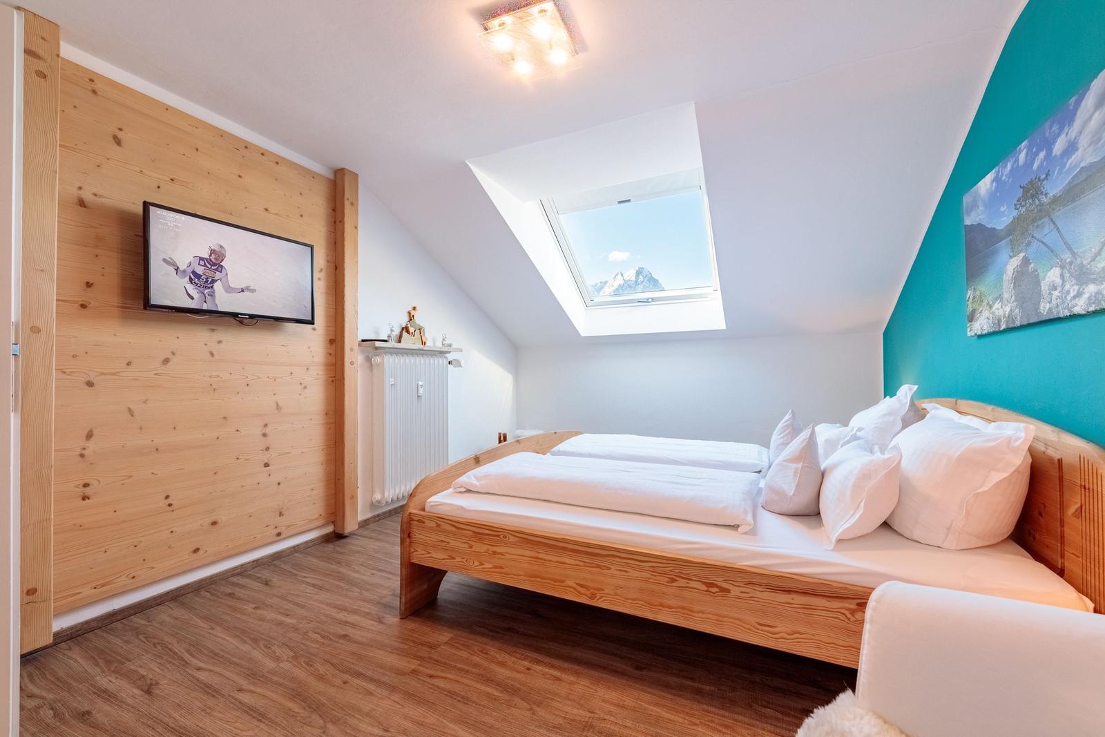 Schlafzimmer mit Dachfenster, Holzbett und Wandfernseher.