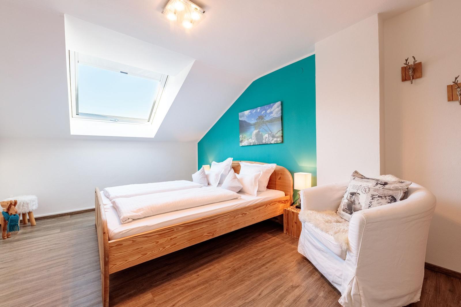 Doppelbett, Sessel, Dachs im Dachzimmer mit Dachfenster und blauer Wand.