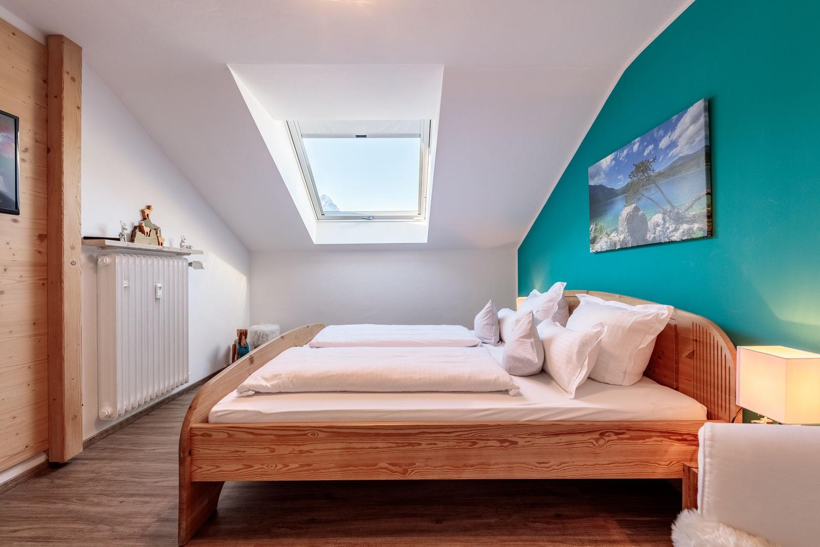Schlafzimmer mit Dachschrägen, Holzbett und Dachfenster. Wand in Türkis mit Landschaftsbild.