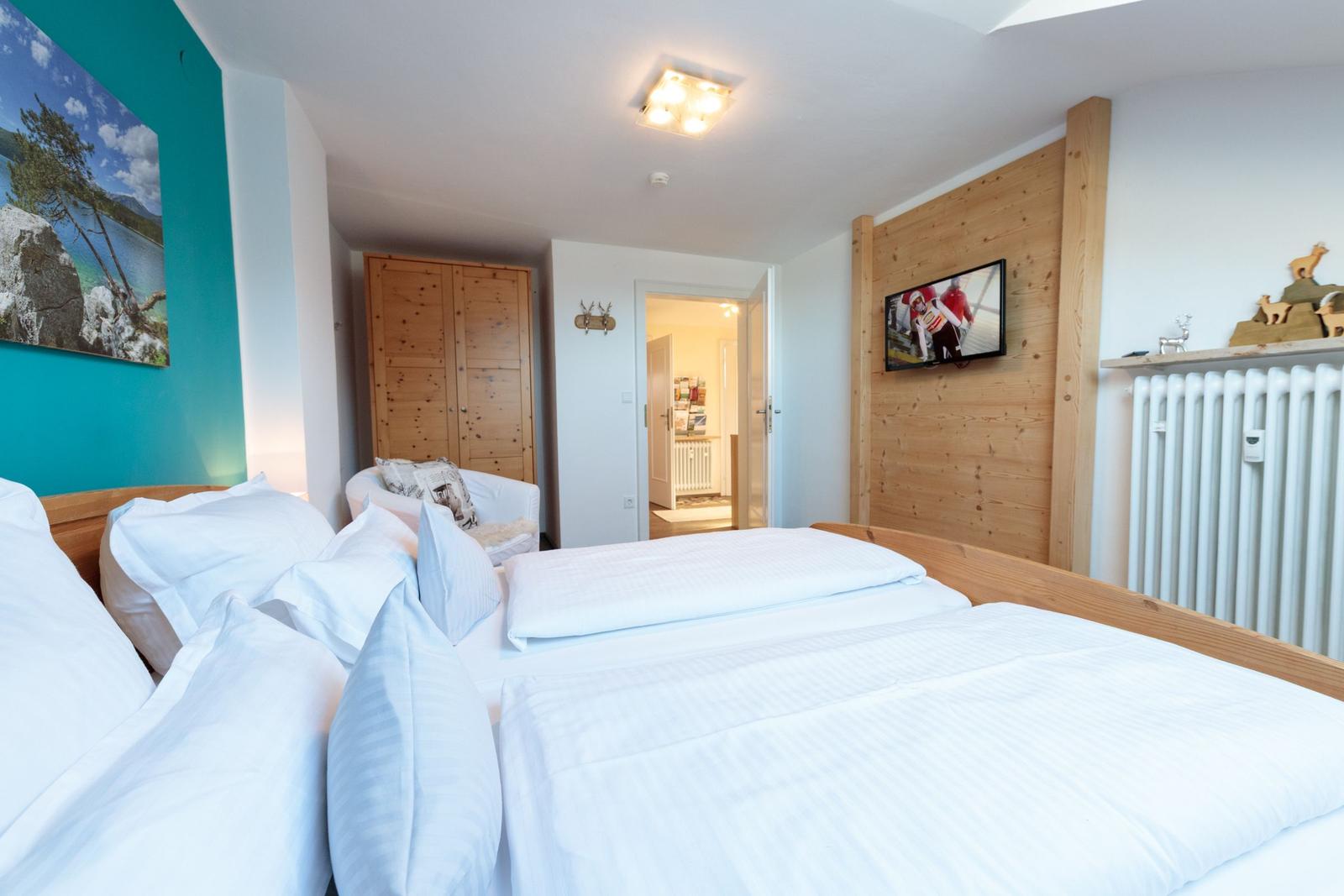 Schlafzimmer mit Bett, Fernseher und Holzwand