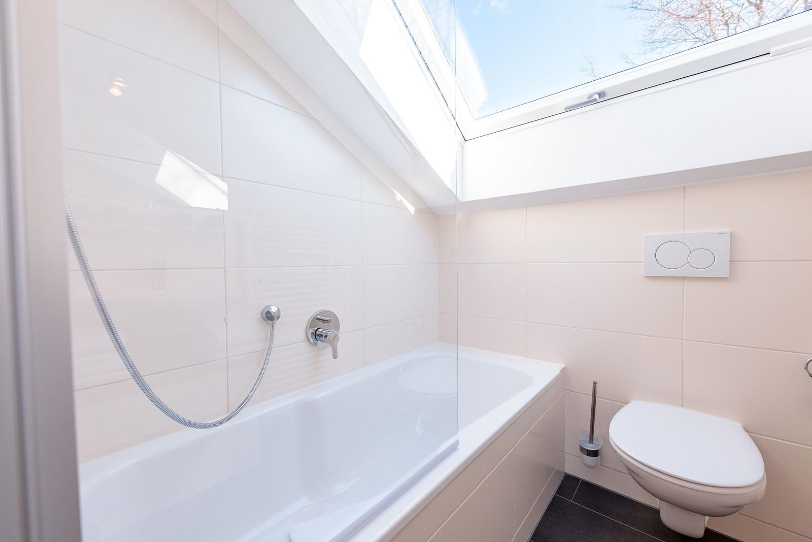 Badezimmer mit Badewanne, Duschbrause und Toilette unter Dachschrägen.